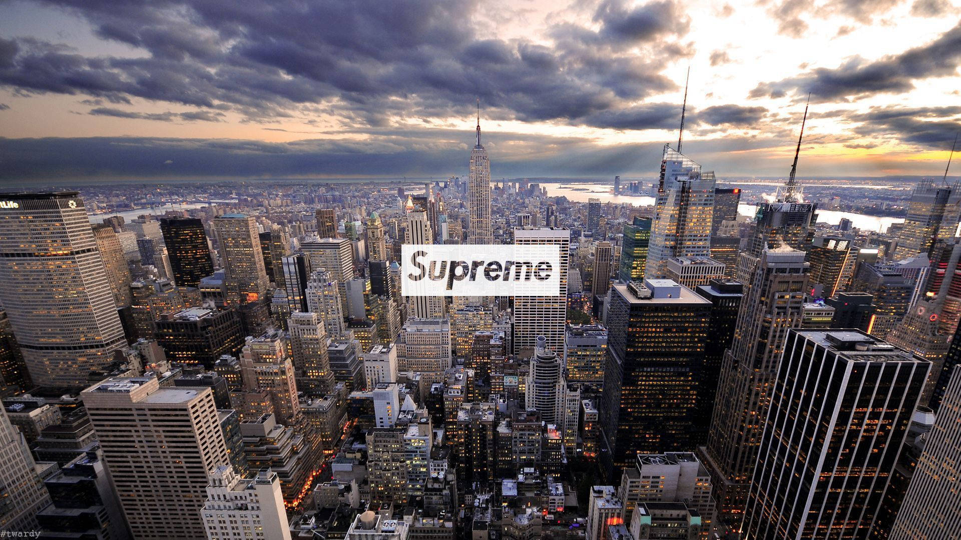 酷炫 Supreme 紐約日落 壁紙 — 紐約市天際線在黃昏時的戲劇性鳥瞰圖，雲層和燈火通明的摩天大樓上疊加著Supreme標誌。