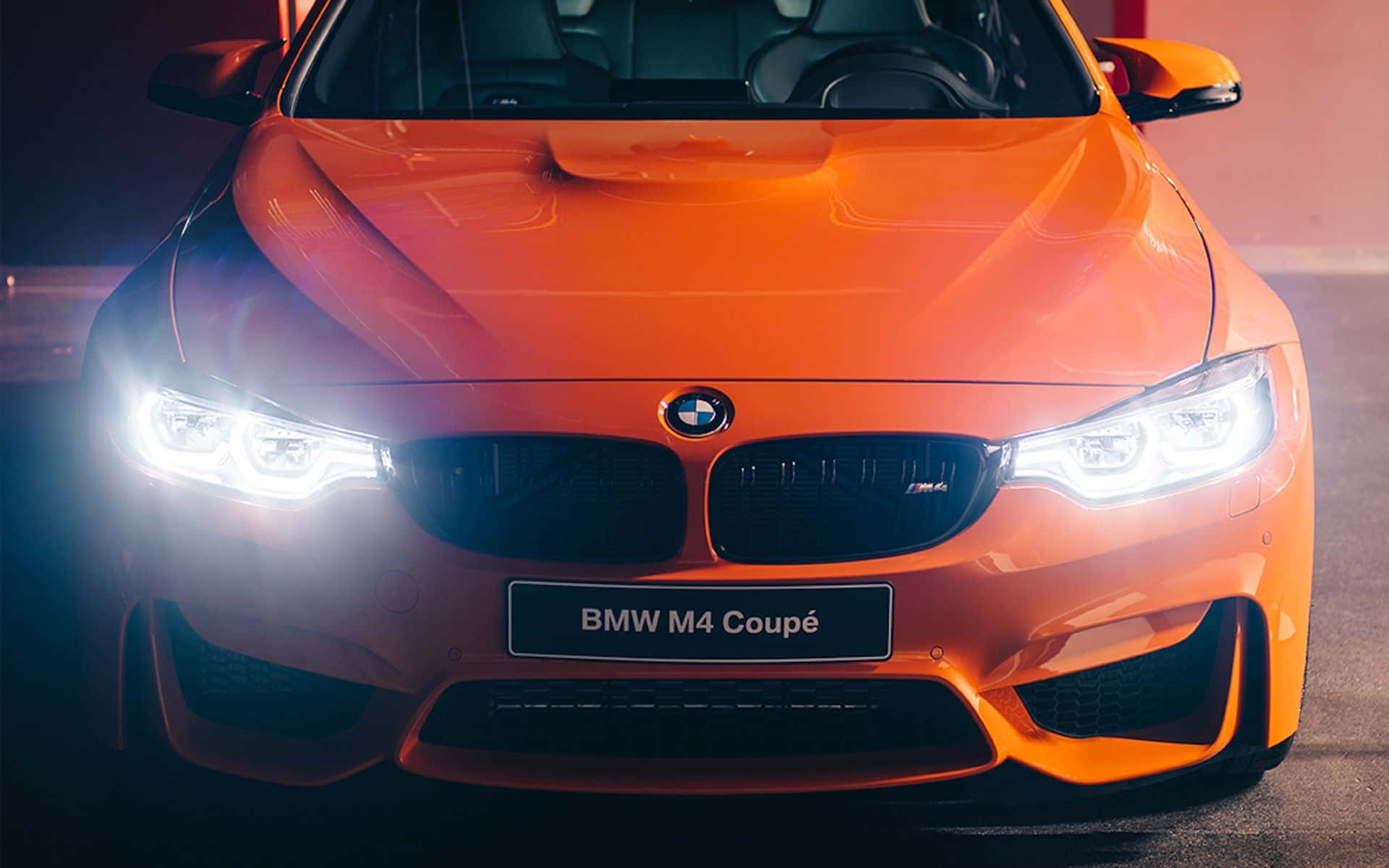 在黑暗環境中帶有發光車頭燈的橙色BMW M4雙門轎跑車。