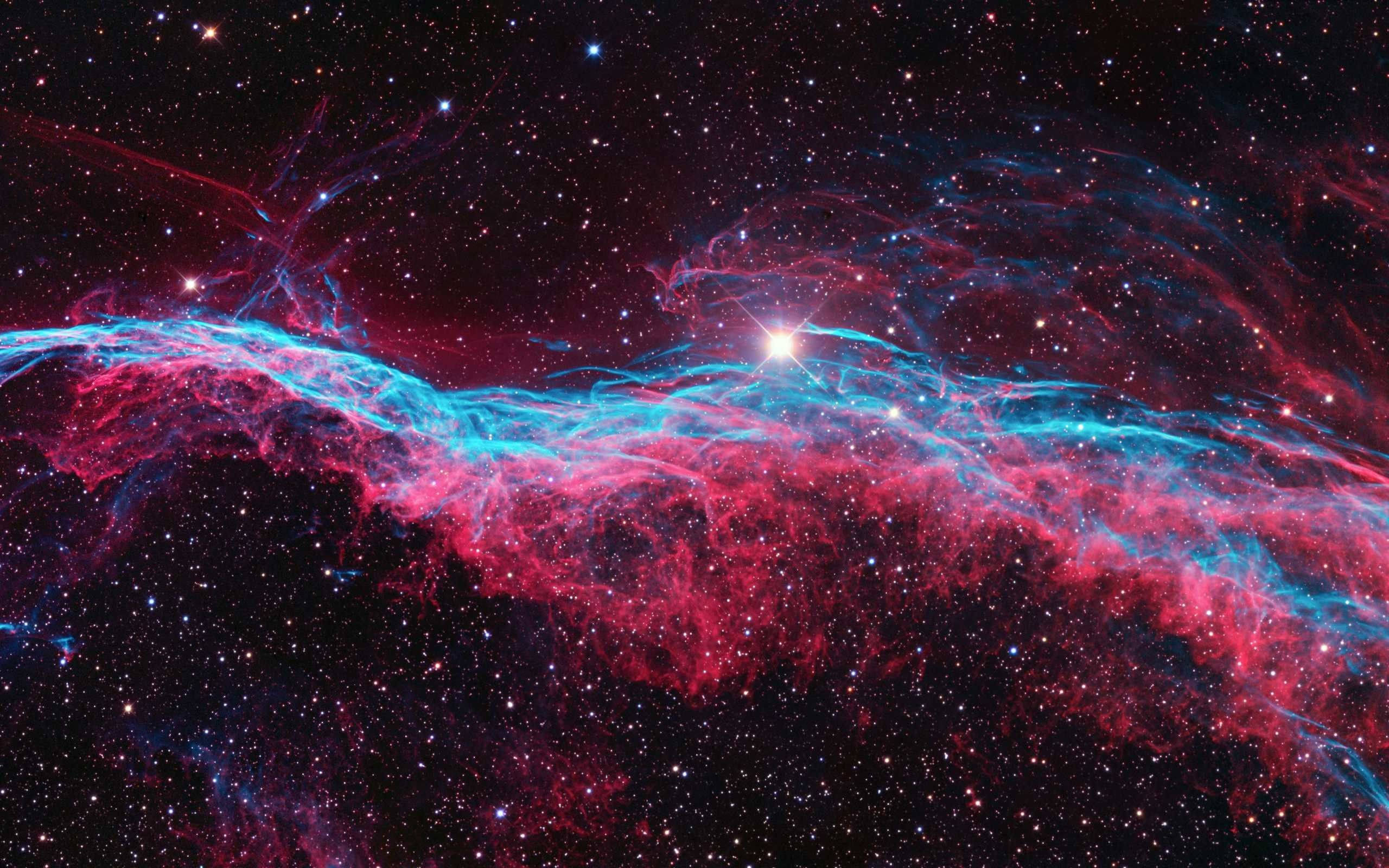 酷炫星系星塵 壁紙 — 一個宇宙星雲以鮮豔的紅色和電光藍色旋轉，背景是星空，一顆明亮的中央恆星照亮了宇宙塵埃。