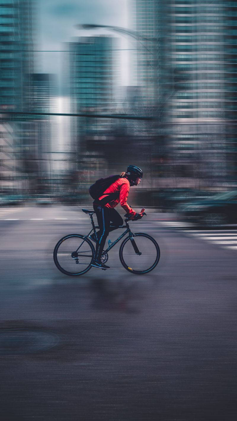 紅色外套單車手在模糊摩天大樓的城市街道上快速騎行。