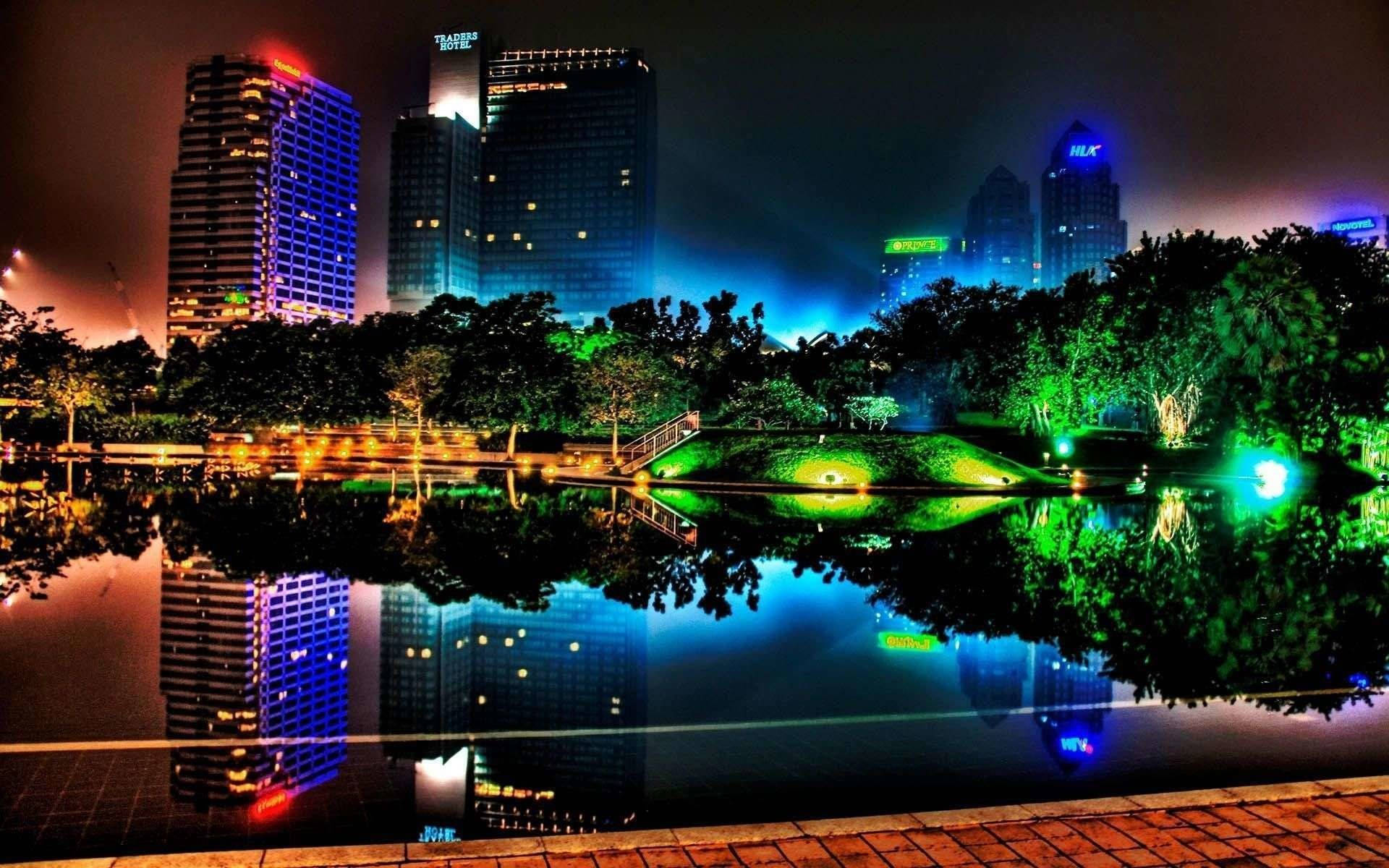 霓虹城市天際線倒映在夜晚寧靜的池塘中，周圍環繞著發光的綠色樹木。