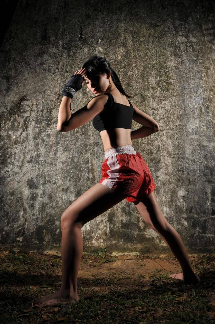 身穿紅色短褲和黑色上衣的運動型女性，對著混凝土牆擺出武術姿勢。