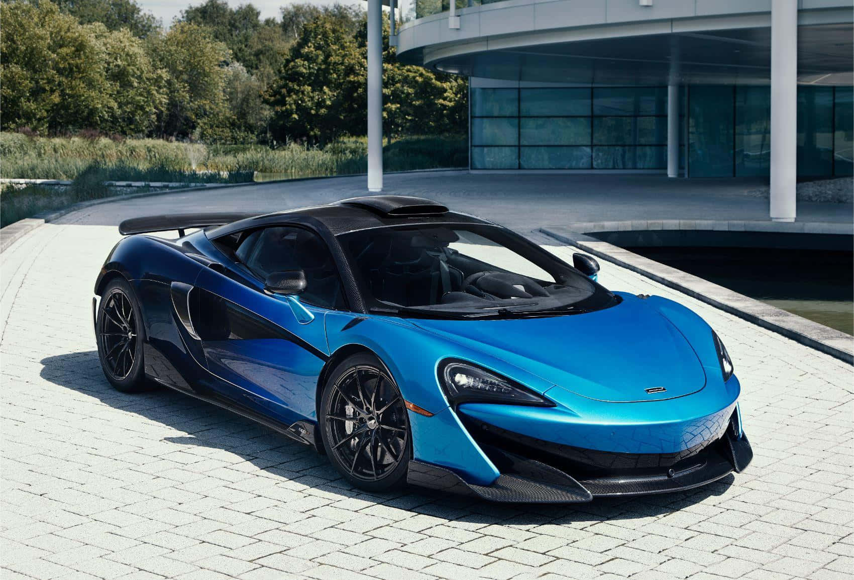 藍色McLaren跑車停泊在現代玻璃建築附近的鋪砌車道上。