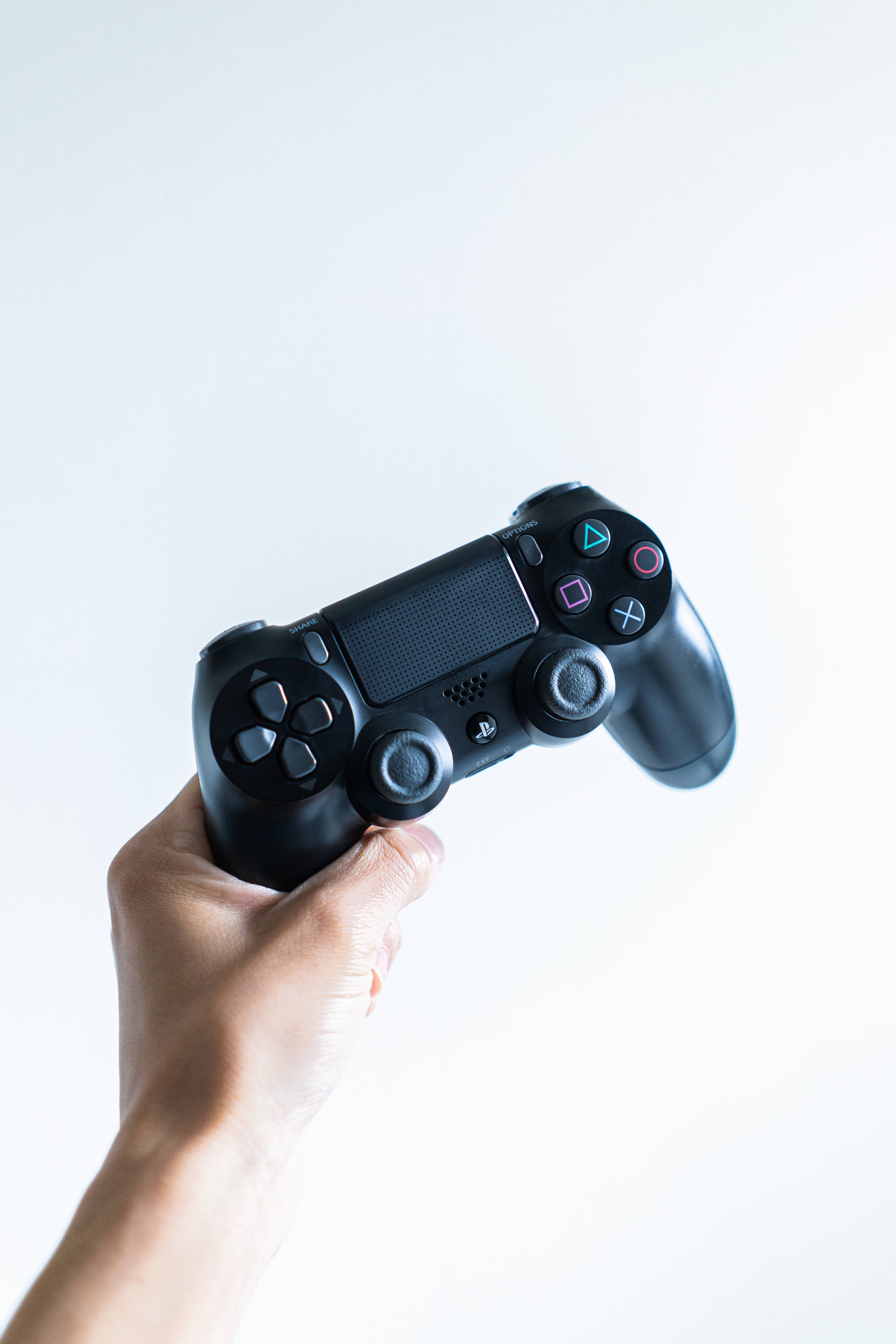 酷炫遊戲PS4控制器 壁紙 — 一隻手在明亮的白色背景上握著一個黑色PlayStation控制器。