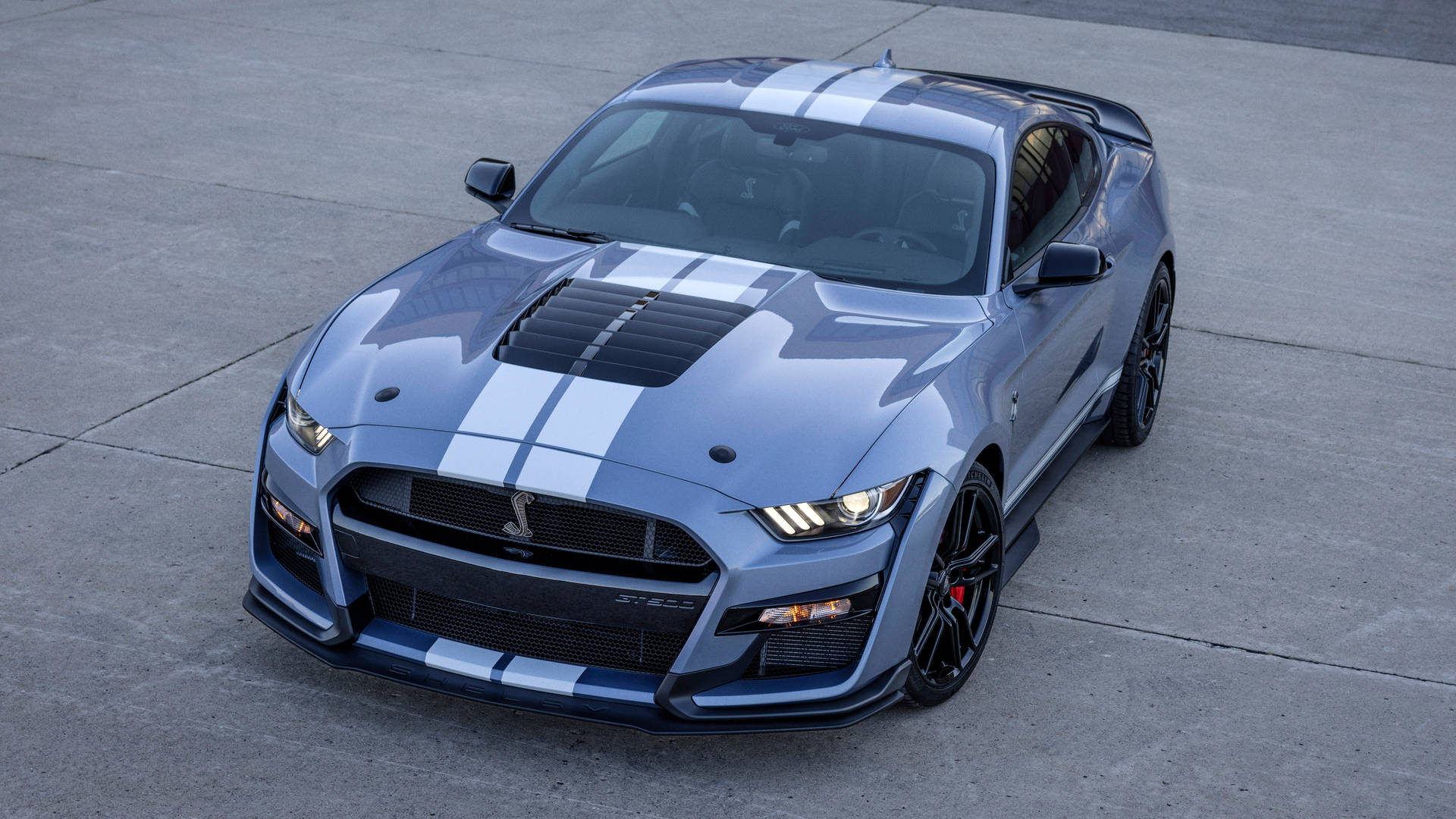 銀色Shelby GT500跑車帶有白色賽車條紋，停在混凝土上。