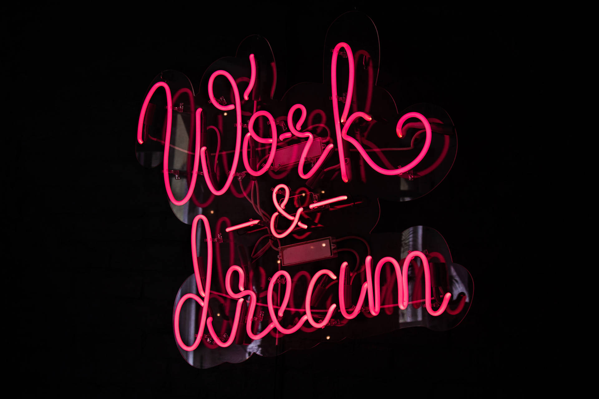 粉紅色霓虹燈牌，上面寫著 Work & Dream，掛在深色牆上。