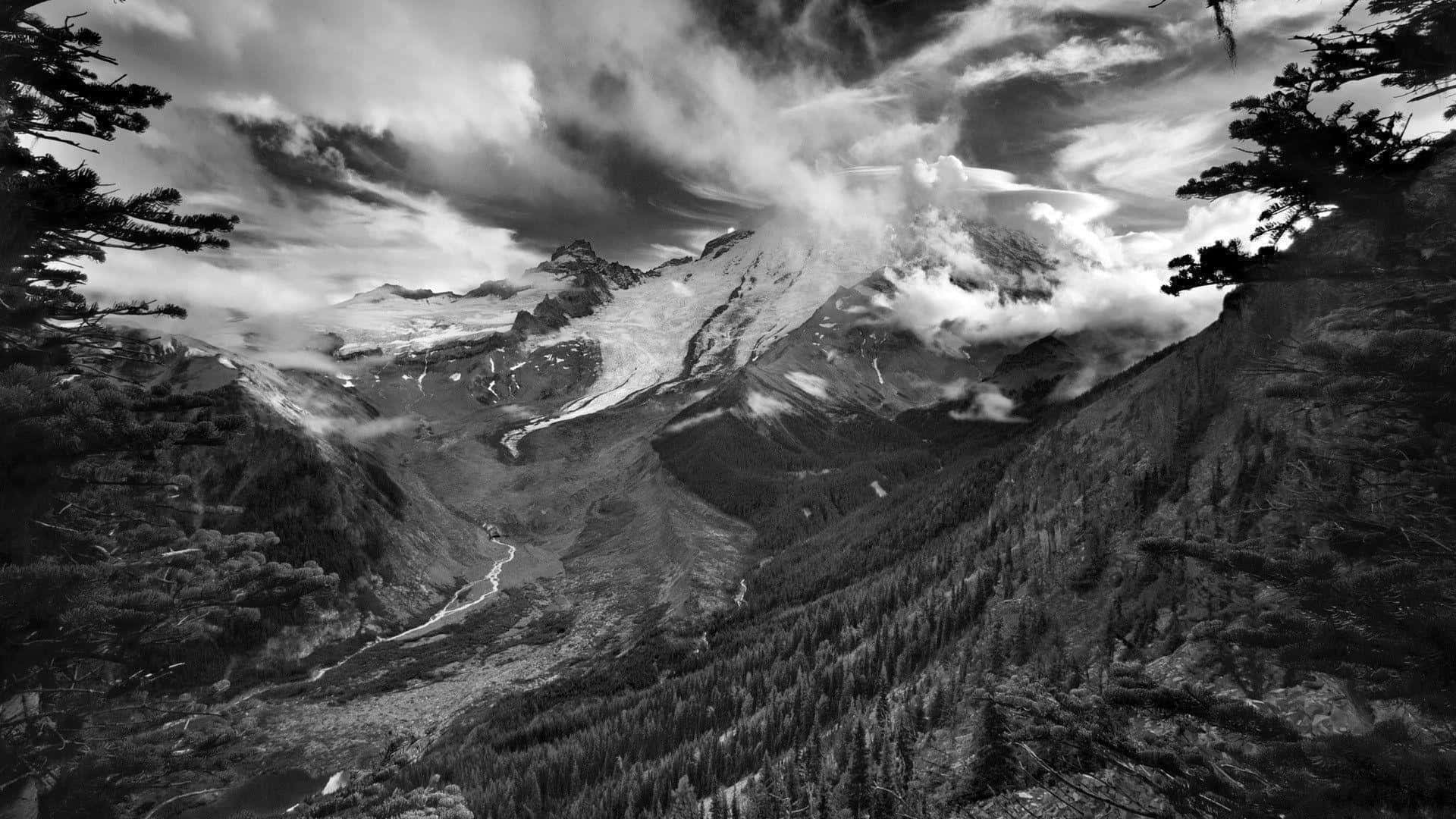 酷炫黑白山景圖片 壁紙 — 一個戲劇性的黑白山景，有白雪覆蓋的山峰、旋轉的雲霧，以及蜿蜒穿過森林山谷的河流。