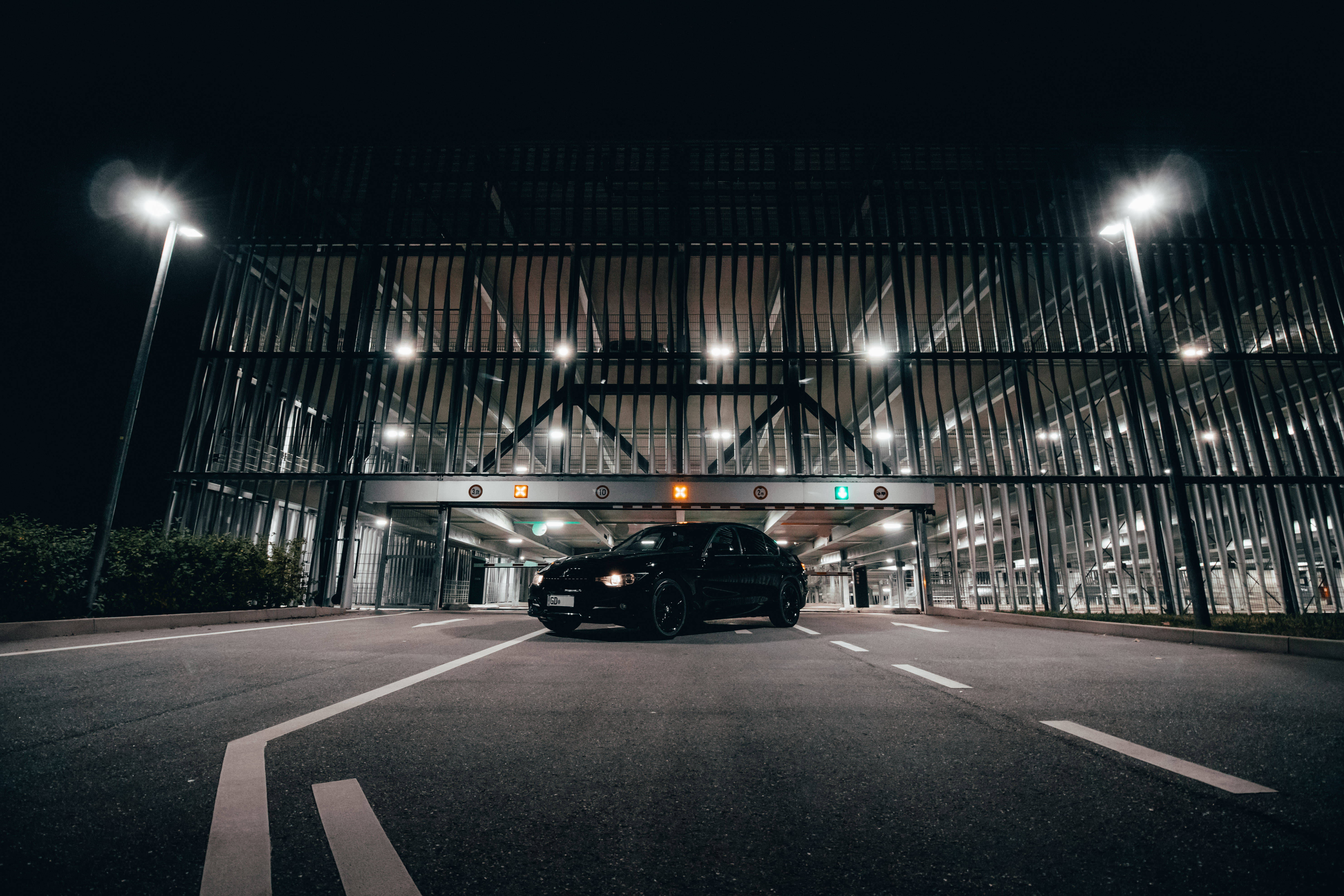 酷炫黑色BMW M系列 壁紙 — 一輛時尚的黑色汽車在夜間停放在現代金屬結構下，明亮的街燈投下戲劇性的陰影。