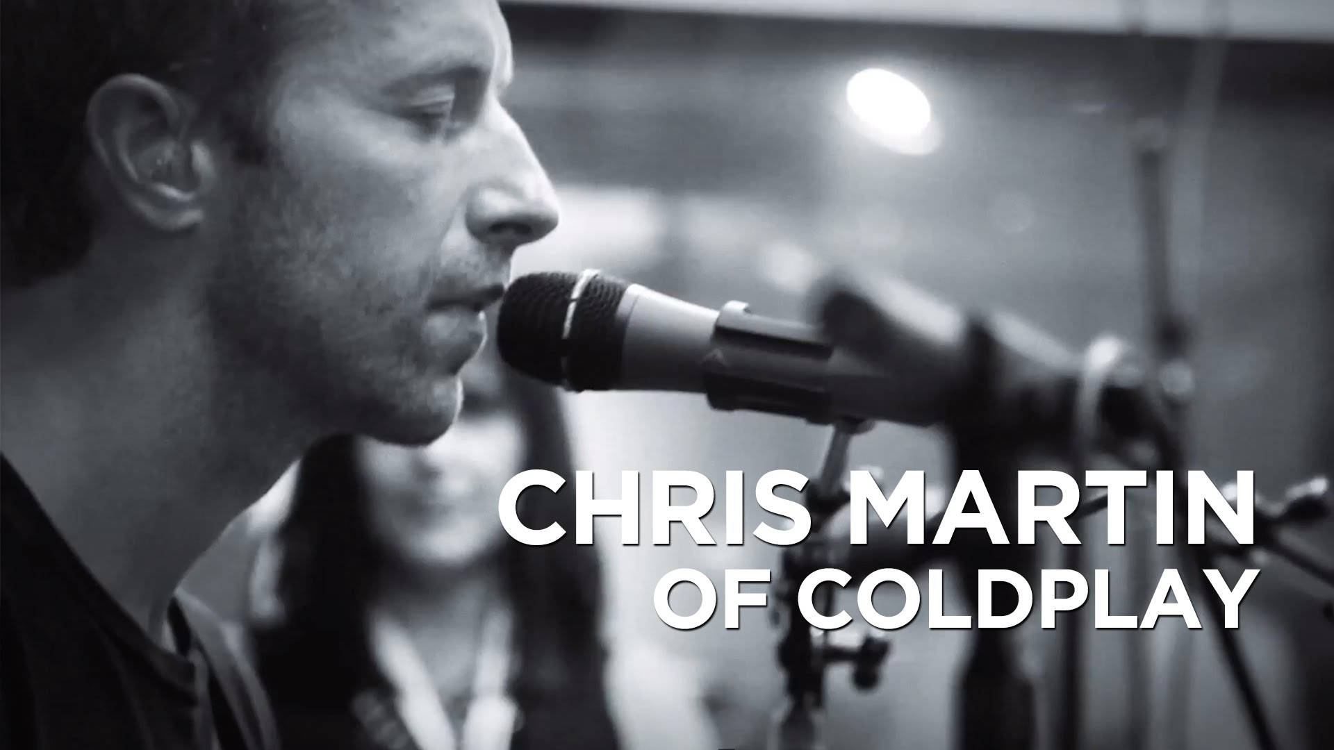 酷玩樂隊主唱克里斯·馬汀 壁紙 — Coldplay 的 Chris Martin 在光線昏暗、柔和燈光及模糊背景的錄音室中對著麥克風唱歌。