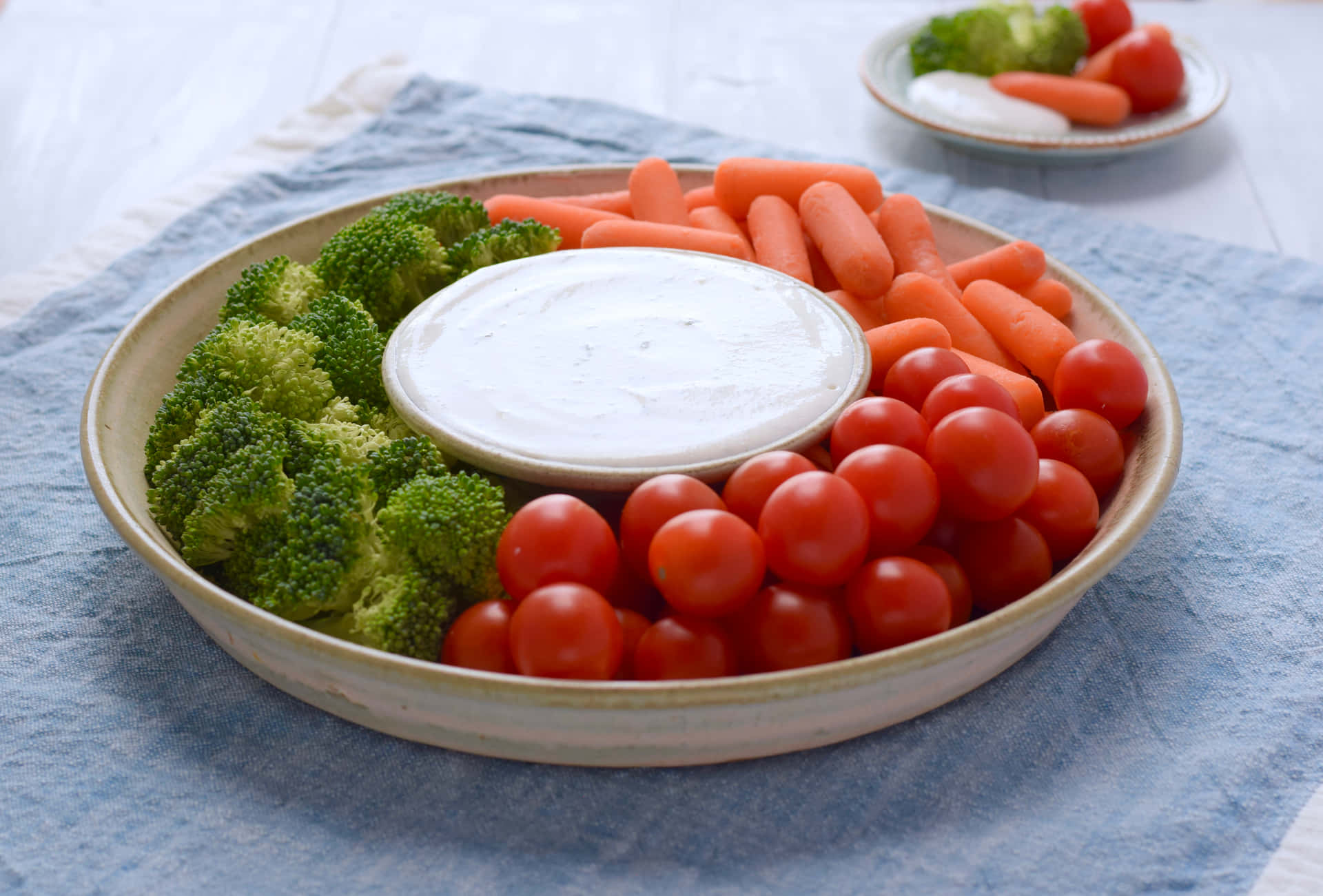 一碗新鮮蔬菜配蘸醬，放在藍色布上。