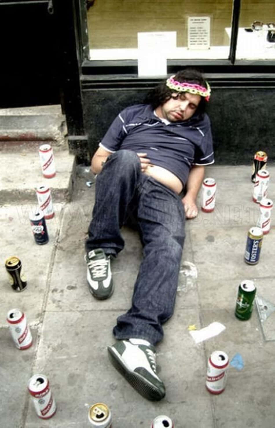 醉酒啤酒挑戰梗圖 壁紙 — 一個戴著彩色頭帶的男人睡在人行道上，周圍散落著空啤酒罐。