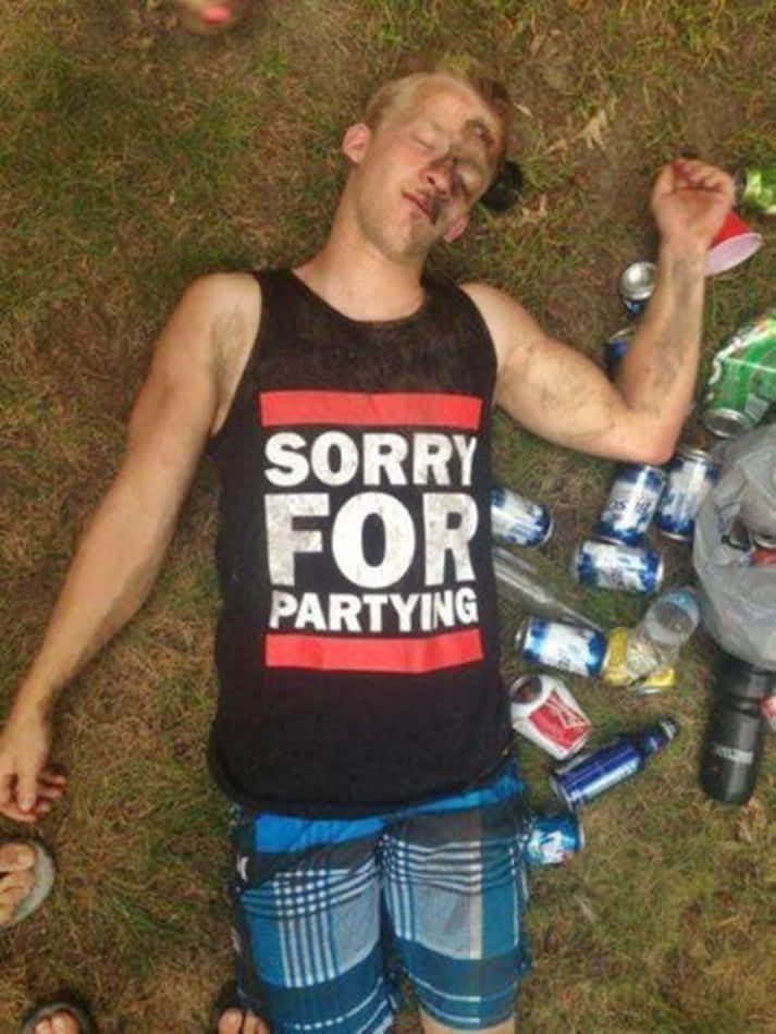 醉酒派對男孩圖 壁紙 — 一個穿著「Sorry For Partying」背心的年輕男子躺在草地上睡著了，周圍散落著空啤酒罐和杯子。