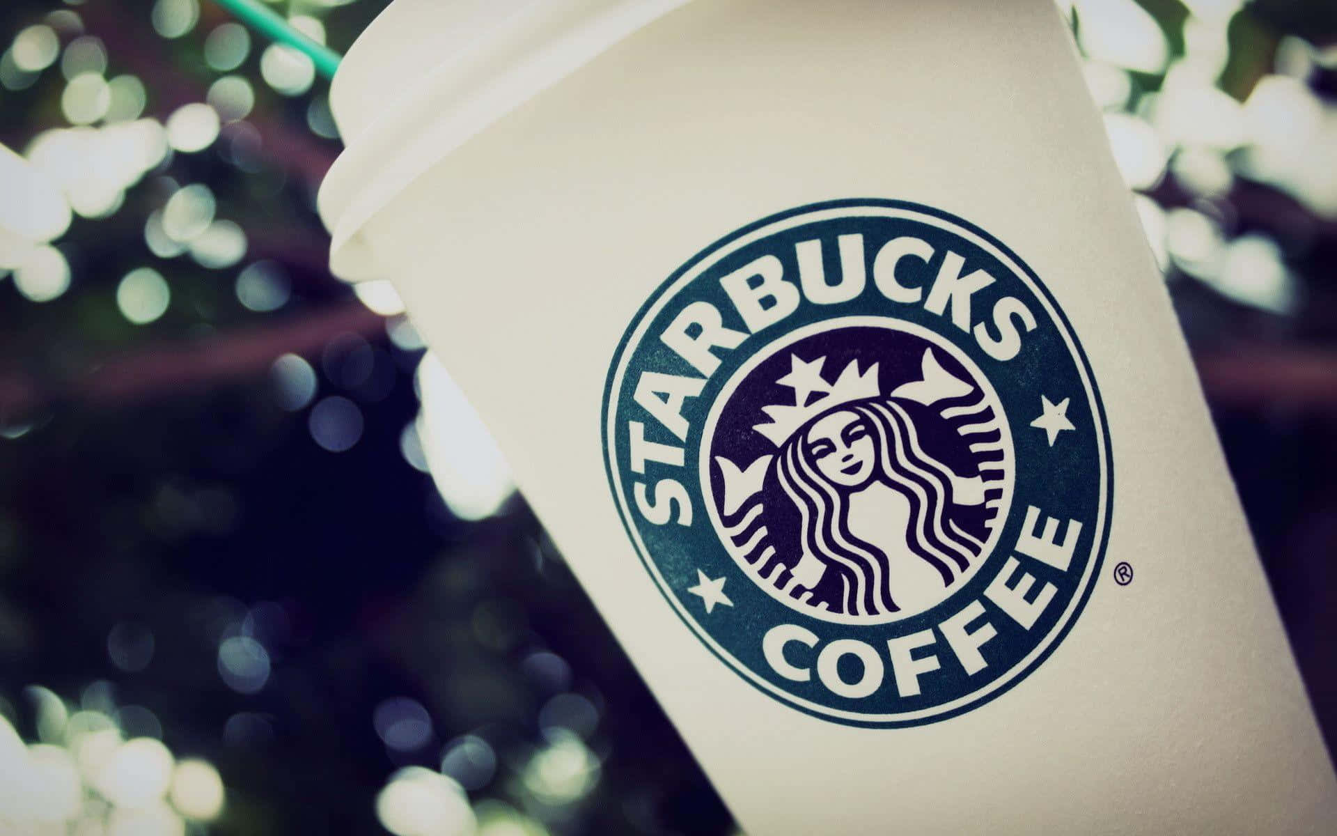 一個Starbucks咖啡杯，標誌清晰，背景是模糊的綠色樹葉。