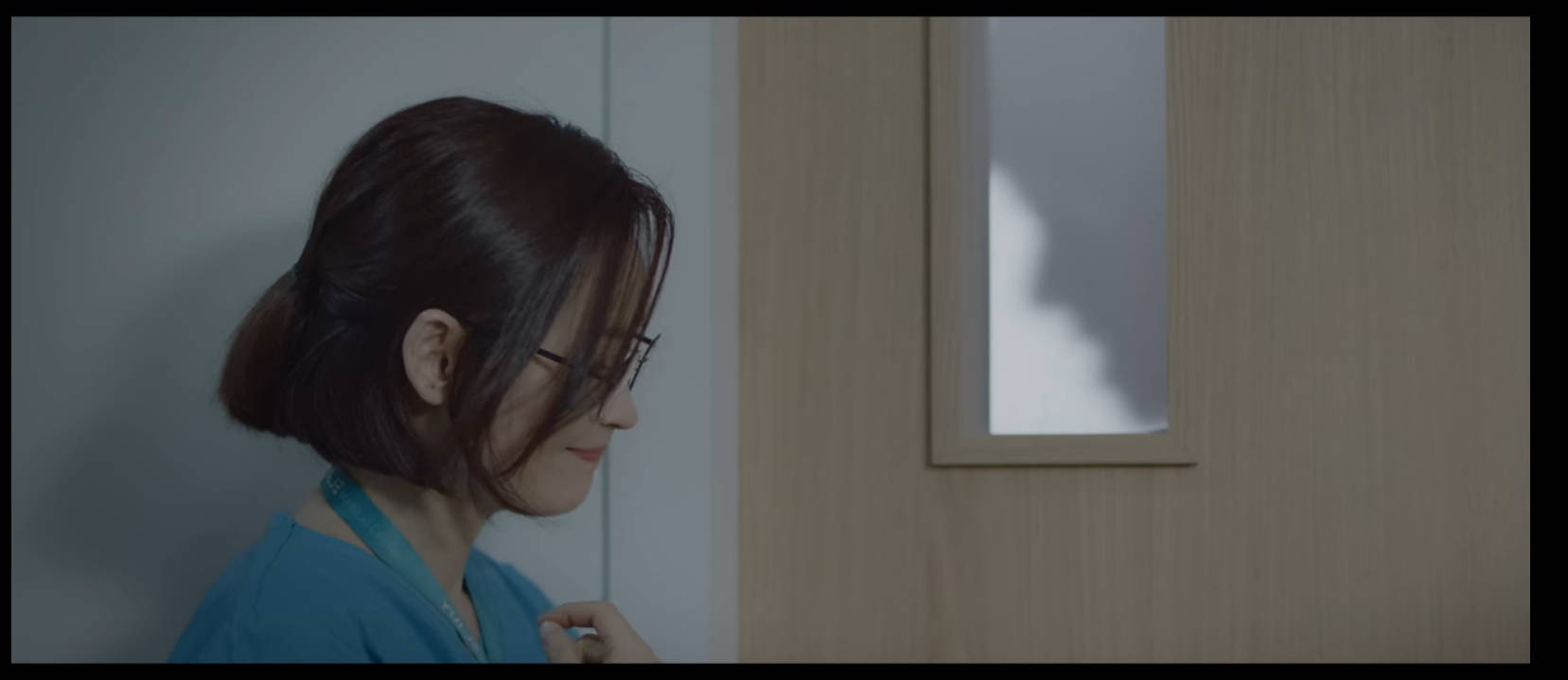 醫院播放清單 松華門口 壁紙 — 一位身穿藍色制服嘅女士企喺門旁邊，身後牆上投射出陰影。