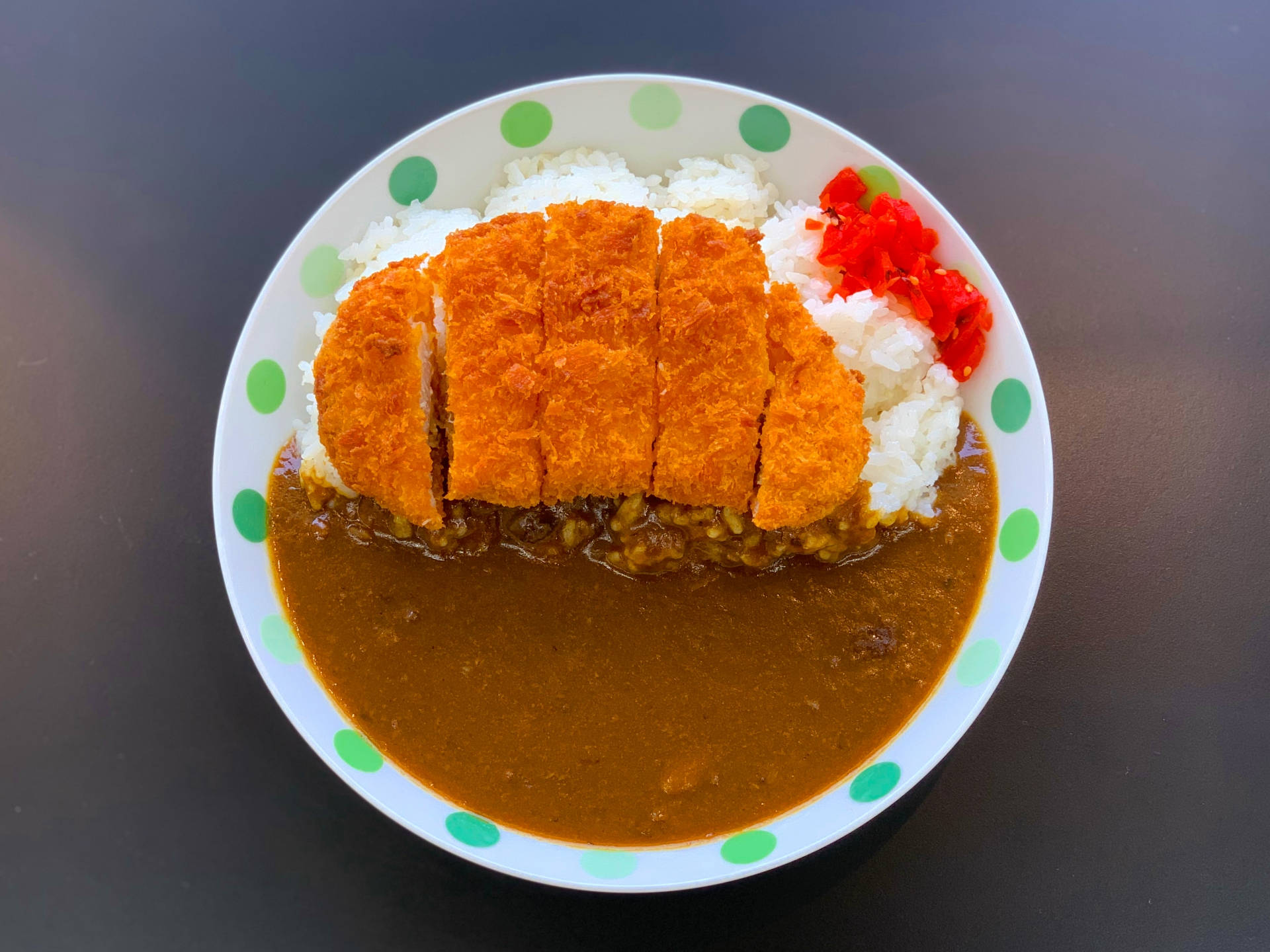 醬汁豐盛的無骨豬排 壁紙 — 一碗金黃酥脆的咖喱豬排飯，配上紅色的醃漬生薑和綠色圓點盤子。