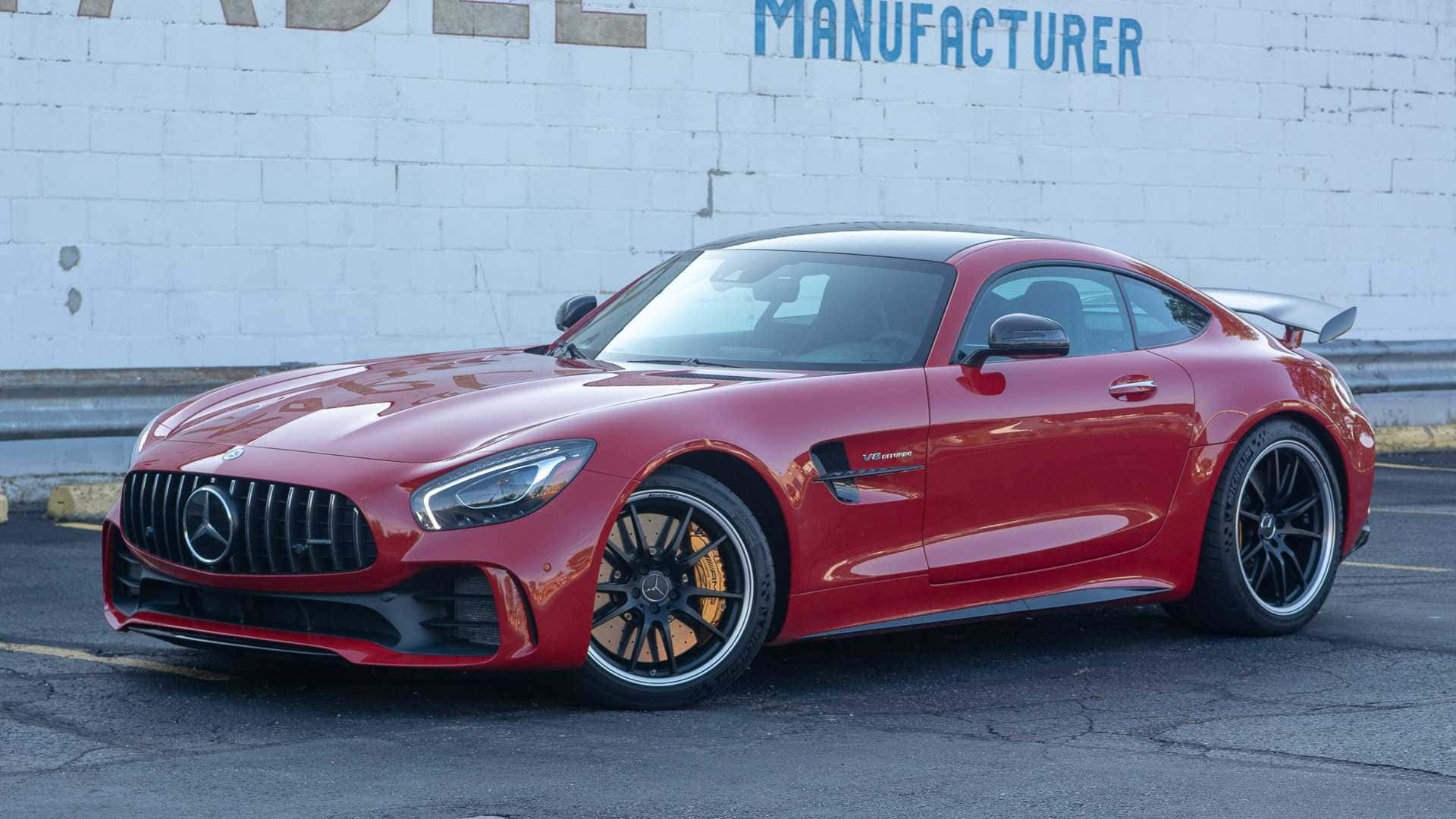 紅色 Mercedes-AMG GT R 跑車停放在磚牆附近的瀝青路面上。
