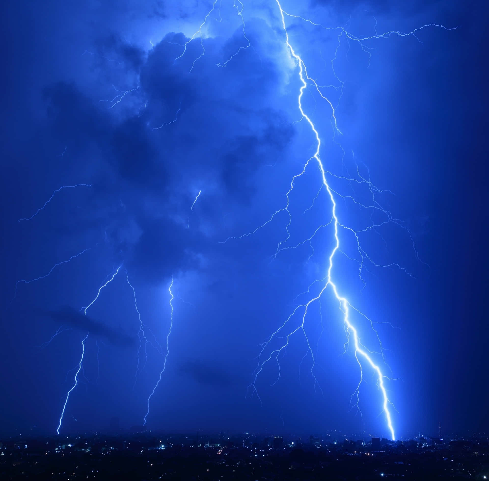 強烈的閃電照亮了夜晚城市上方深藍色的暴風雨天空。