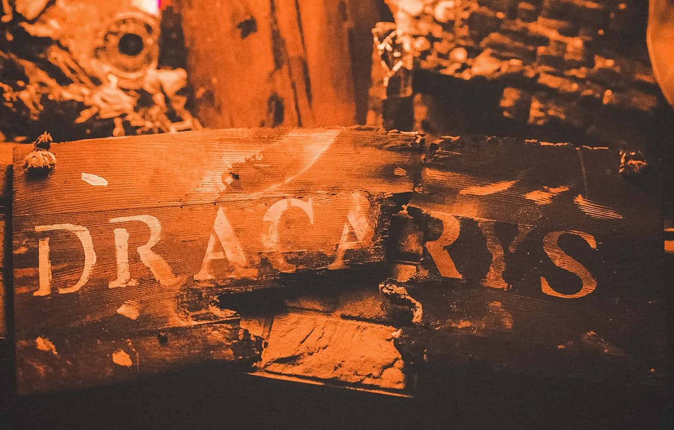 釋放龍焰 - Dracarys 壁紙 — 一塊飽經風霜的木牌，上面剝落的橙色油漆拼出「DRACARIS」，背景是模糊的鄉村風格。
