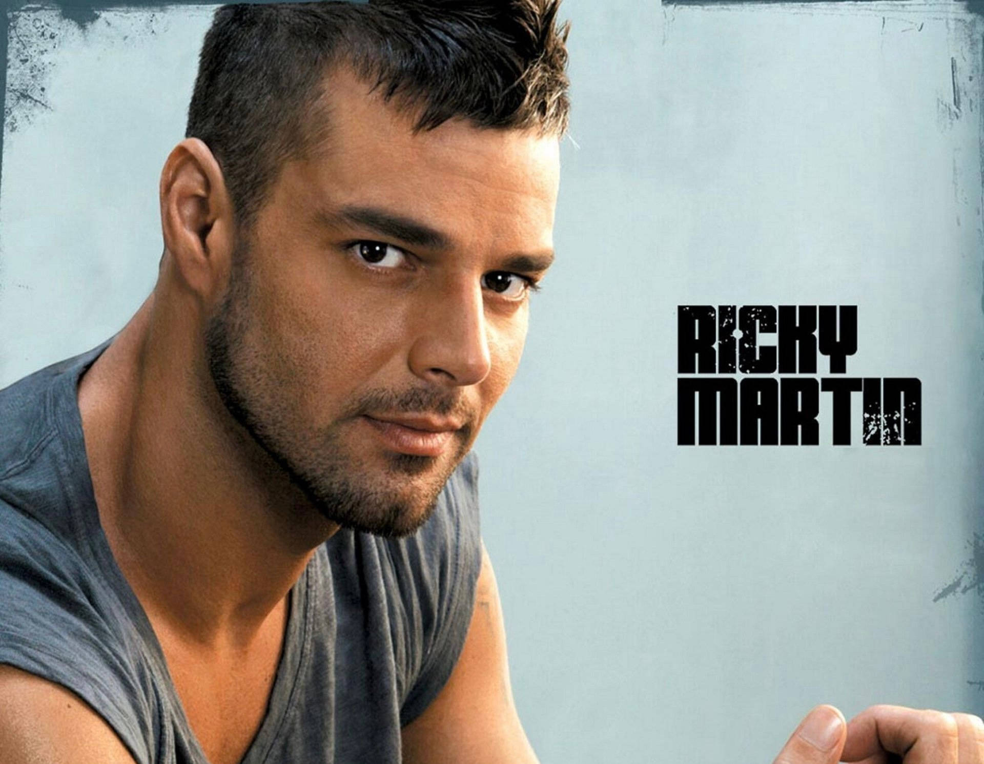 里基·马丁特寫 壁紙 — Ricky Martin 在帶有紋理的淺藍色背景上，以粗體黑色文字，強烈地凝視著觀眾。