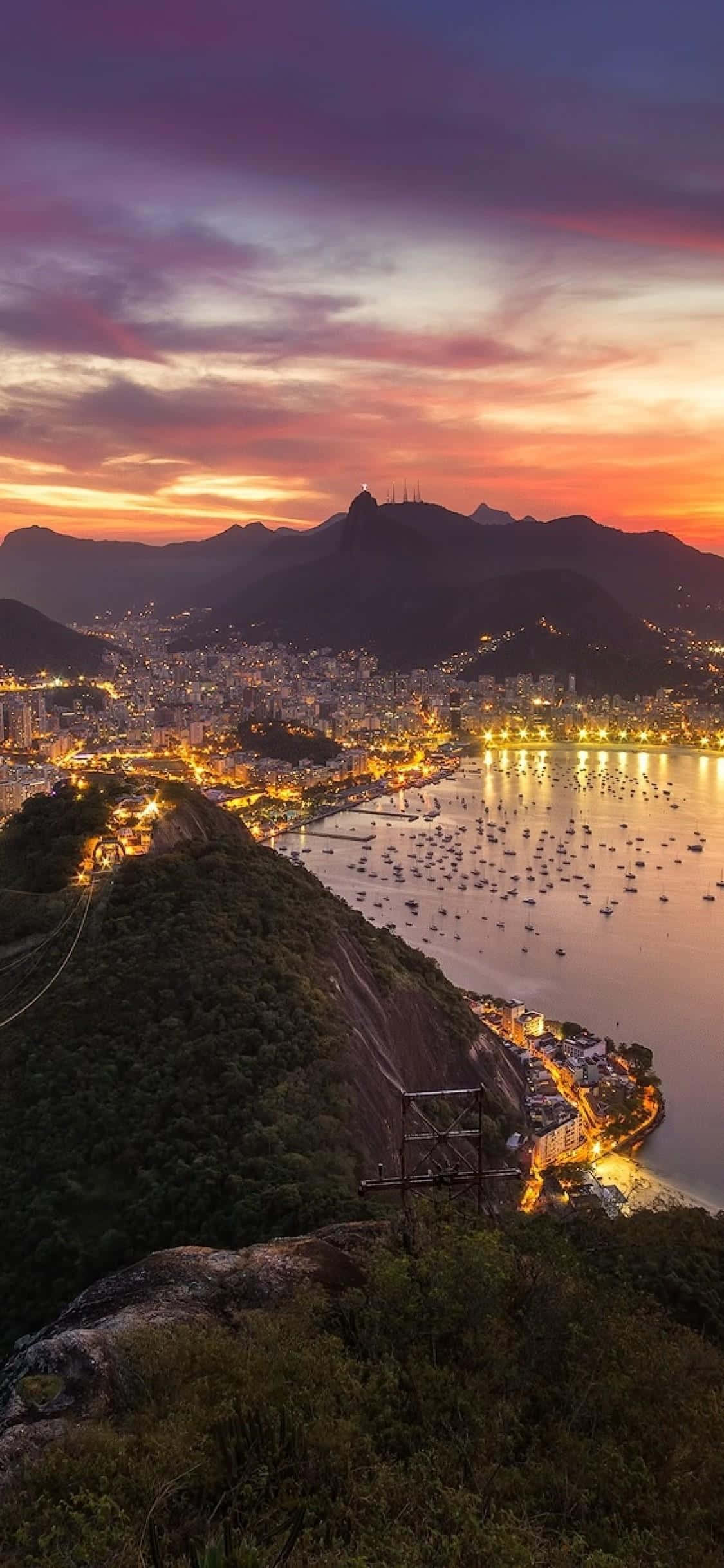 Brazil 桌布 壁紙 — 里約熱內盧令人驚嘆的日落，充滿活力的橙色和紫色天空照亮了城市燈光和山脈。