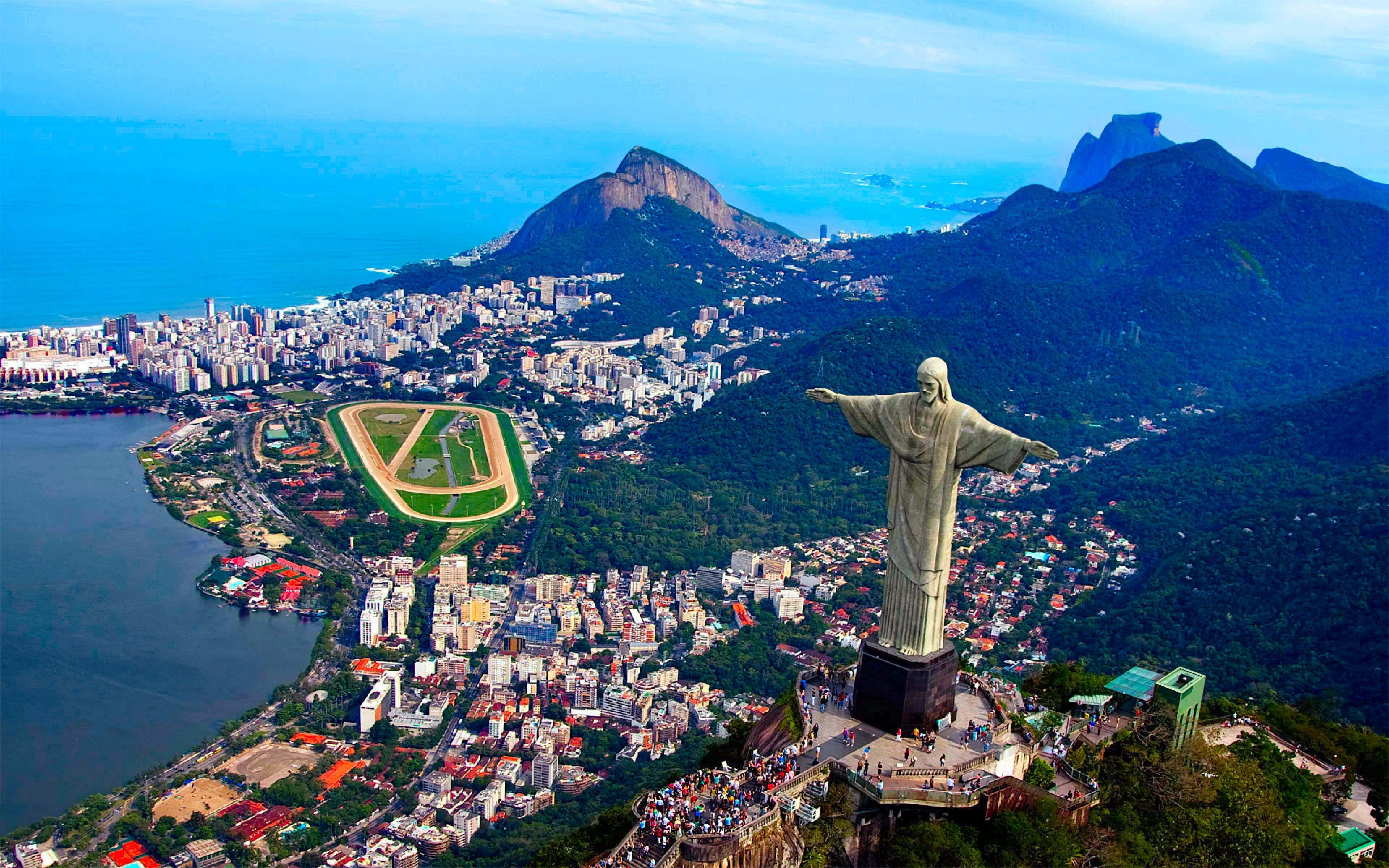 Brazil 桌布 壁紙 — 里約熱內盧的航拍圖，展示基督像俯瞰城市和瓜納巴拉灣，周圍有茂密的山脈和一個賽馬場。