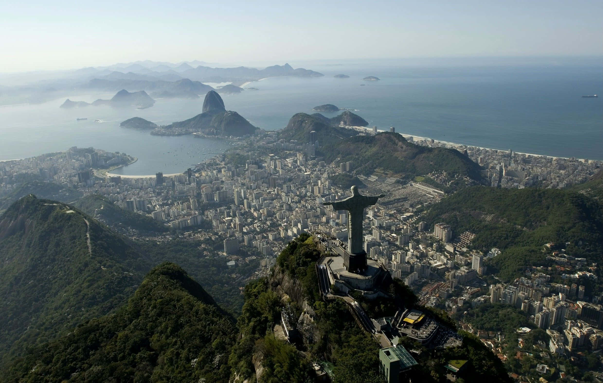 Brazil 桌布 壁紙 — 里約熱內盧的鳥瞰圖，展示基督像俯瞰城市和海洋，遠處有糖麵包山。