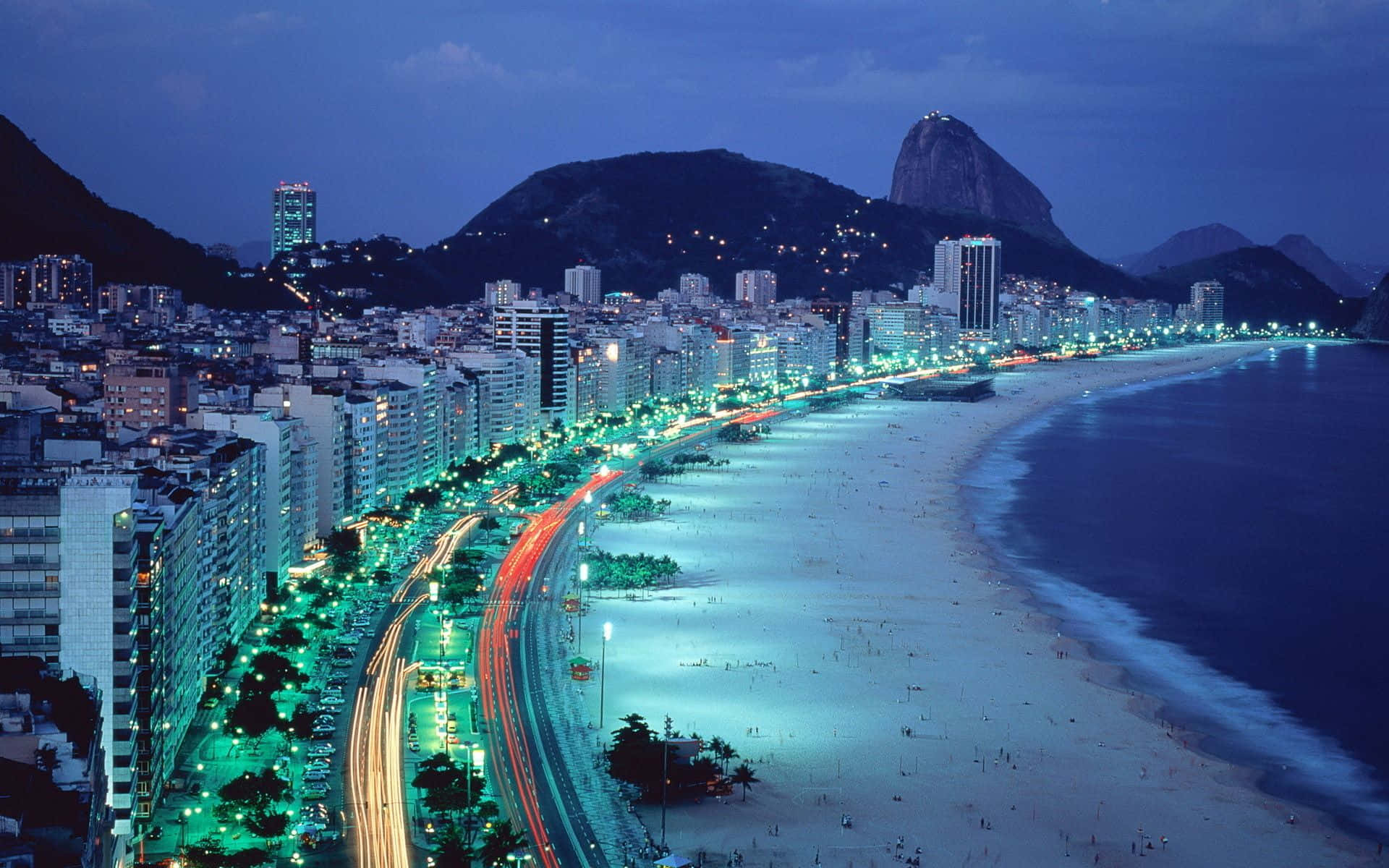 Brazil 桌布 壁紙 — 里約熱內盧科帕卡巴納海灘的活力夜景，閃爍的城市燈光和標誌性的甜麵包山在背景中。