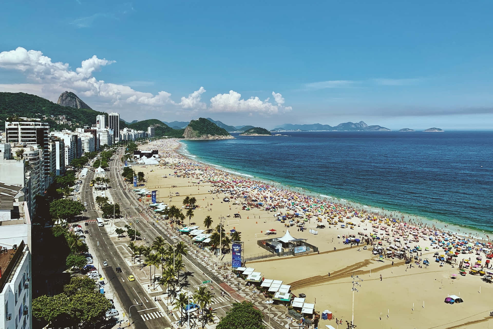 Brazilian Beach 桌布 壁紙 — 里約熱內盧科帕卡巴納海灘的鳥瞰圖，在明亮的藍天和散落的雲朵下，擠滿了享受日光浴的人們。