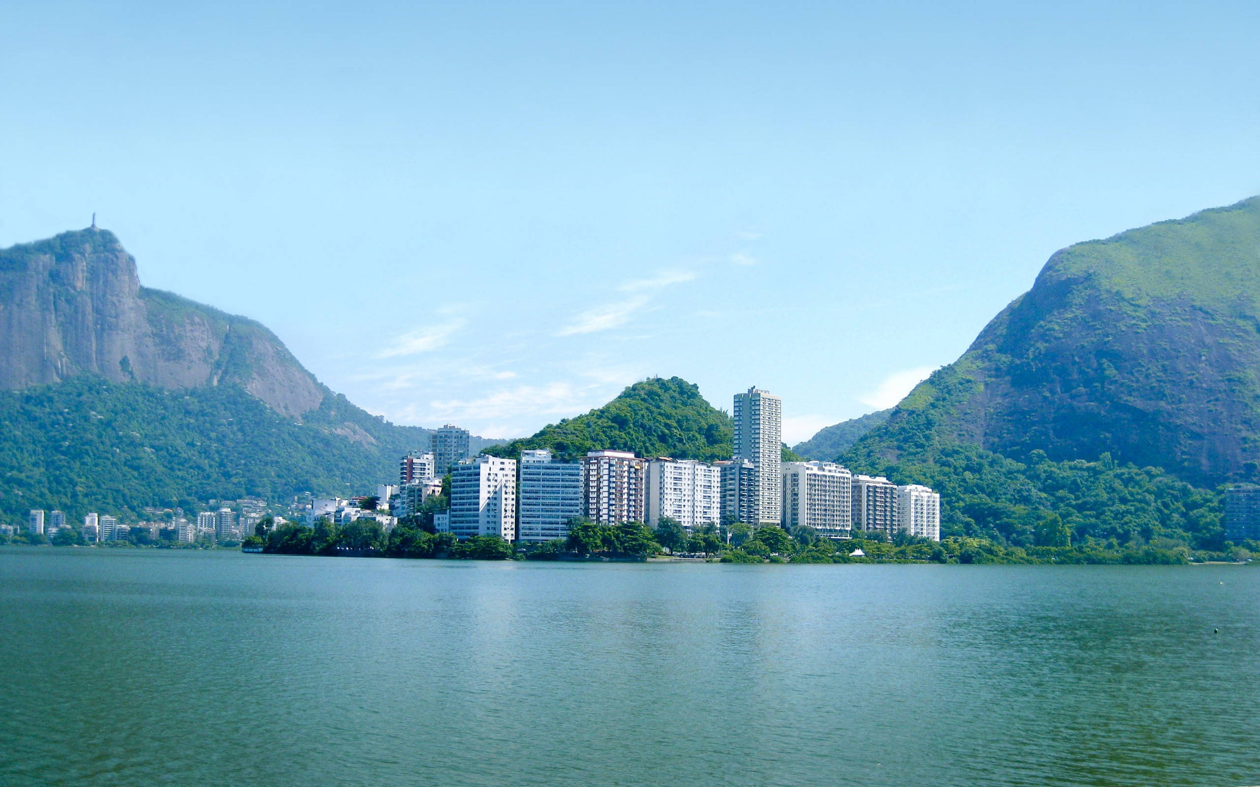 里約熱內盧羅德里戈·德·弗雷塔斯潟湖壯麗景觀 壁紙 — 現代公寓大樓沿著寧靜的綠色湖泊排列，兩側是茂密的山脈，上方是清澈的藍天。