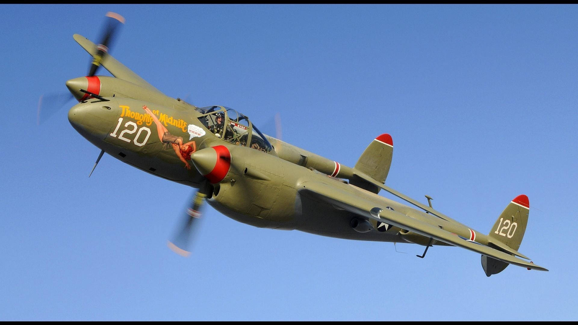 重型二戰德國戰鬥機 壁紙 — 一架帶有紅色點綴和「Thongy Manik」機頭藝術的復古橄欖綠軍用飛機在清澈的藍天中翱翔。