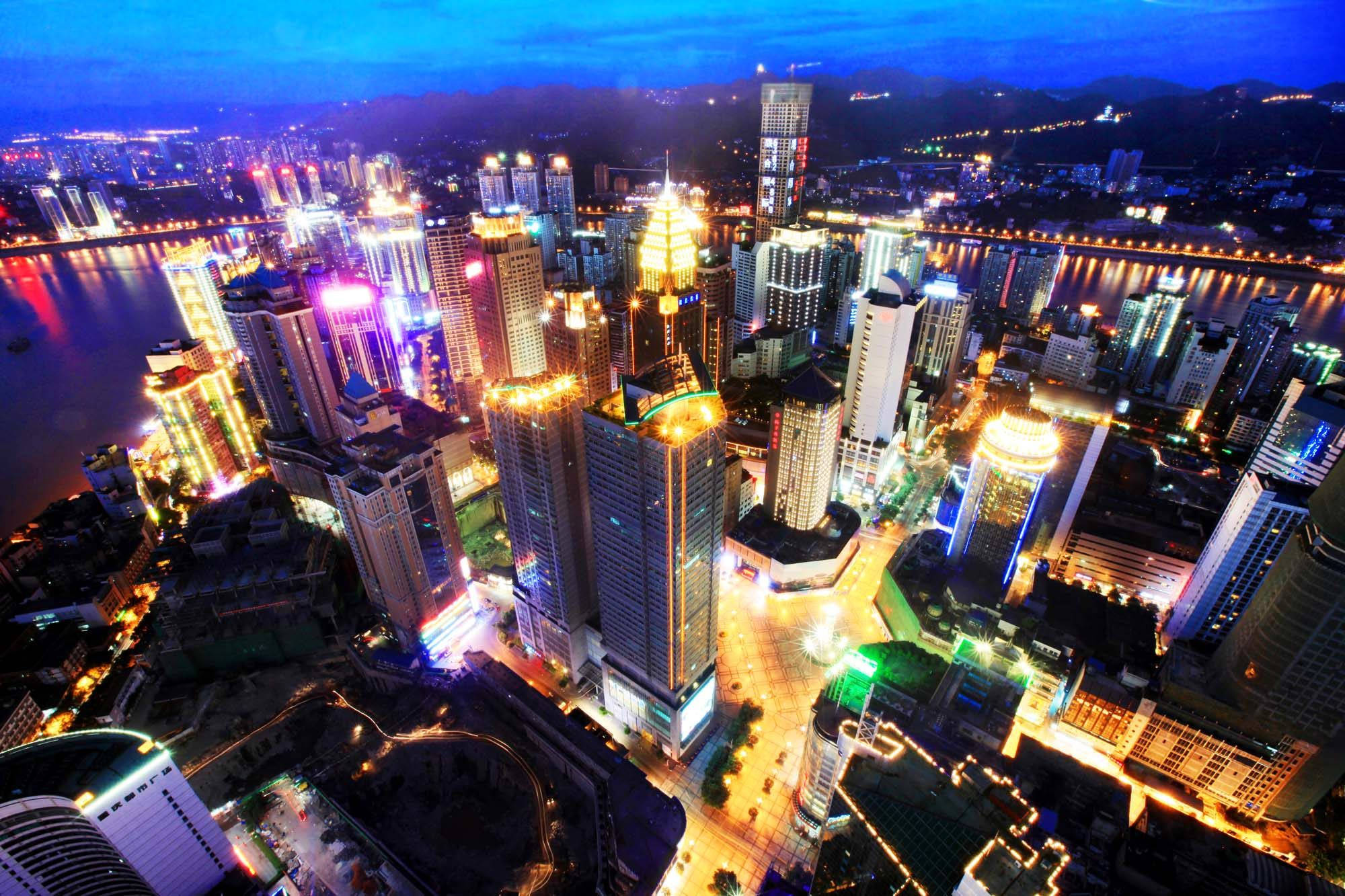 重慶中國城市燈光 壁紙 — 黃昏時分充滿活力的城市景觀鳥瞰圖，霓虹燈照亮的摩天大樓倒映在河面上。