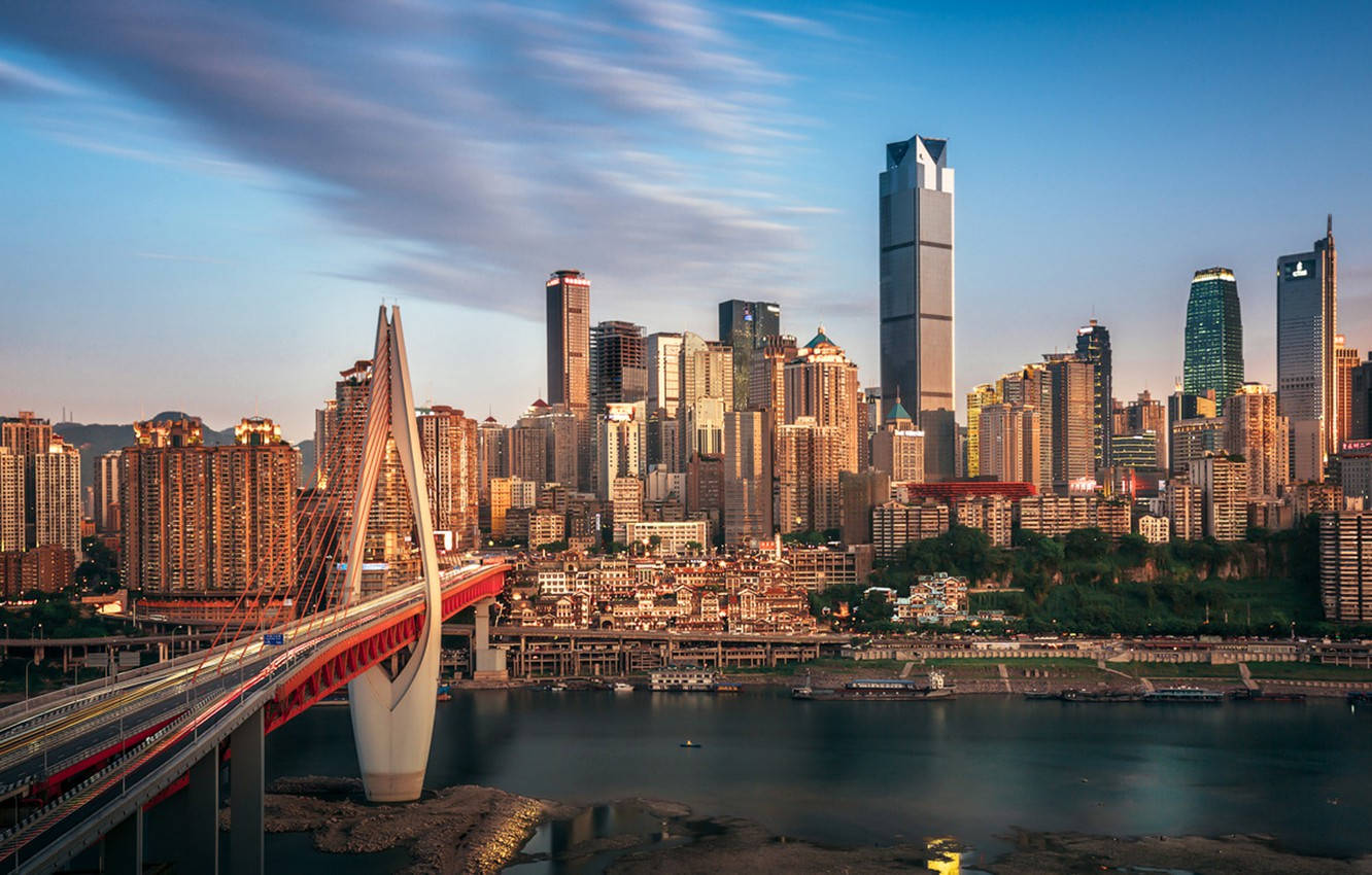 重慶中國復古城市風景 壁紙 — 日落時分充滿活力的城市景觀，一座醒目的紅色橋樑橫跨河流，高聳的摩天大樓反射著金色的光芒。