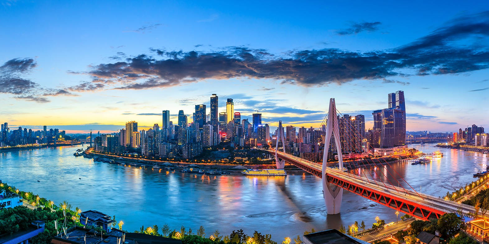 重慶中國日落城市風景 壁紙 — 令人驚嘆的黃昏城市景觀，一座發光的橋樑橫跨寬闊的河流，倒映著摩天大樓和溫暖的燈光。