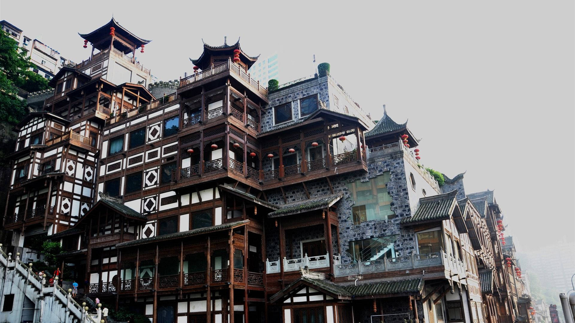 重慶中國洪崖洞建築 壁紙 — 傳統中式木建築，瓦頂和紅燈籠，依附在霧氣瀰漫的山坡上。