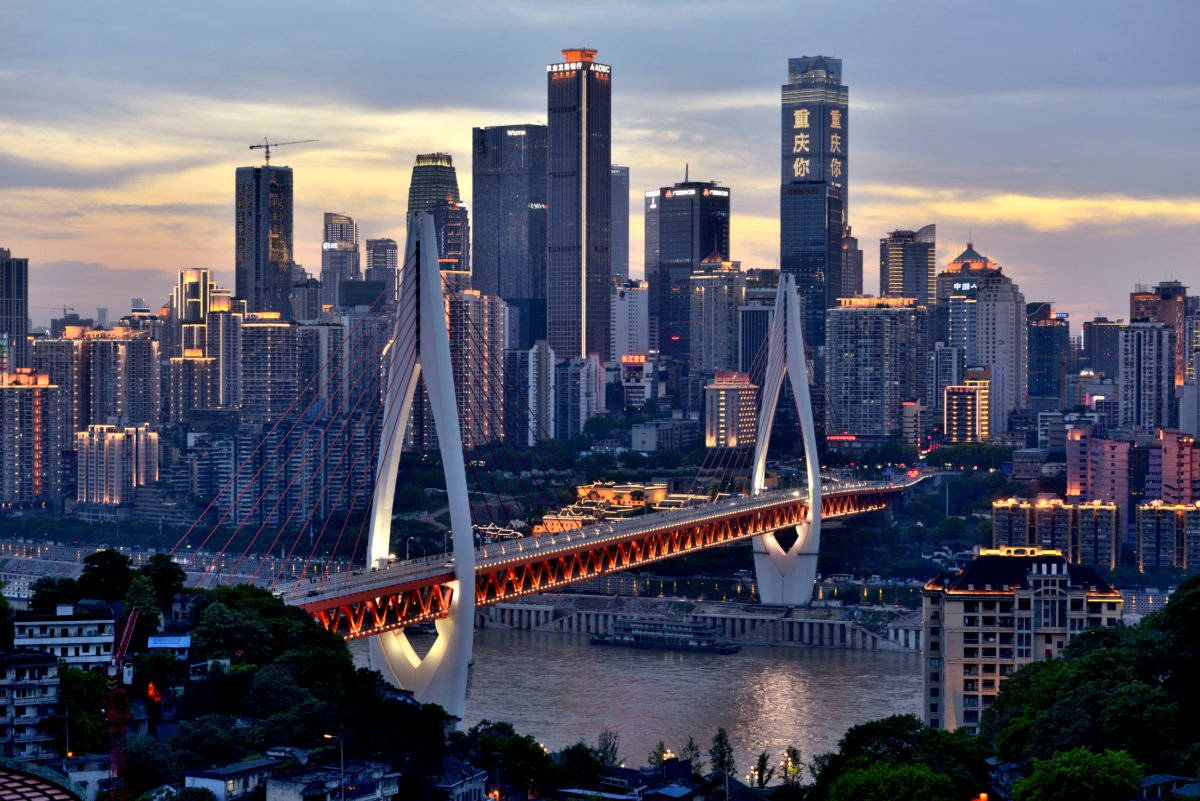 重慶中國空中都市風景 壁紙 — 現代城市景觀的壯麗日落景色，一座發光的斜拉橋橫跨河流，周圍是高聳的摩天大樓。