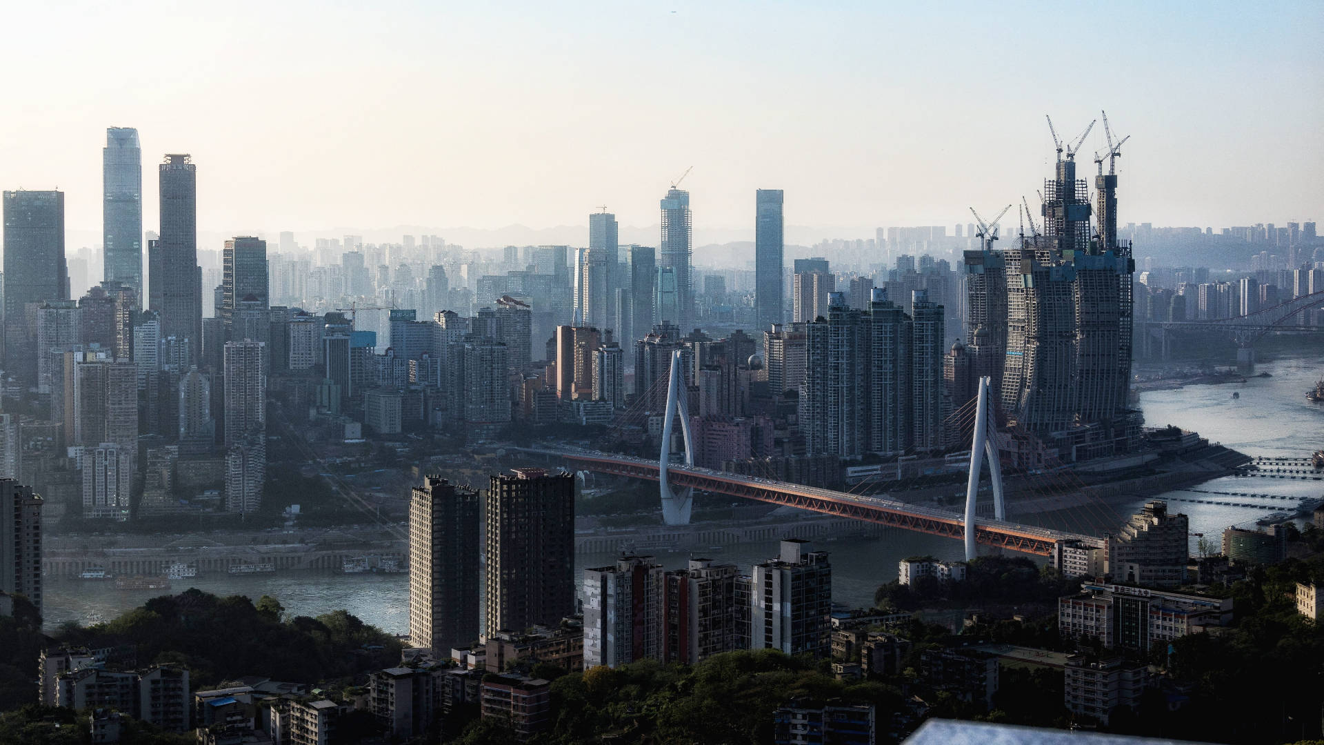 重慶中國褪色城市景觀 壁紙 — 在朦朧的日光下，廣闊的城市天際線，高聳的摩天大樓和一條獨特的曲線橋橫跨寬闊的河流。