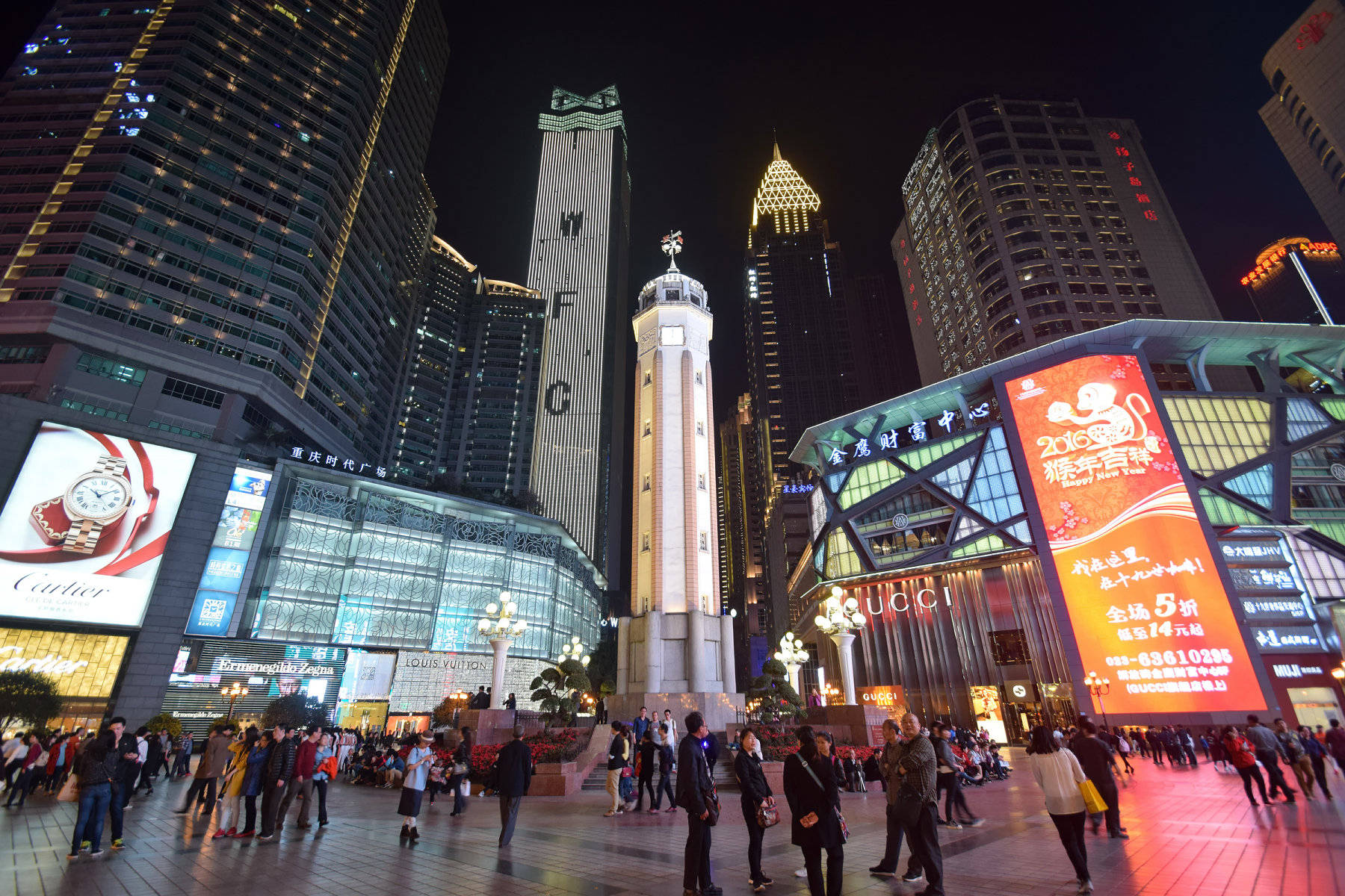 重慶中國解放碑廣場 壁紙 — 一個繁忙的夜間城市廣場，擠滿人群和裝飾著發光廣告牌和霓虹燈的高聳摩天大樓。