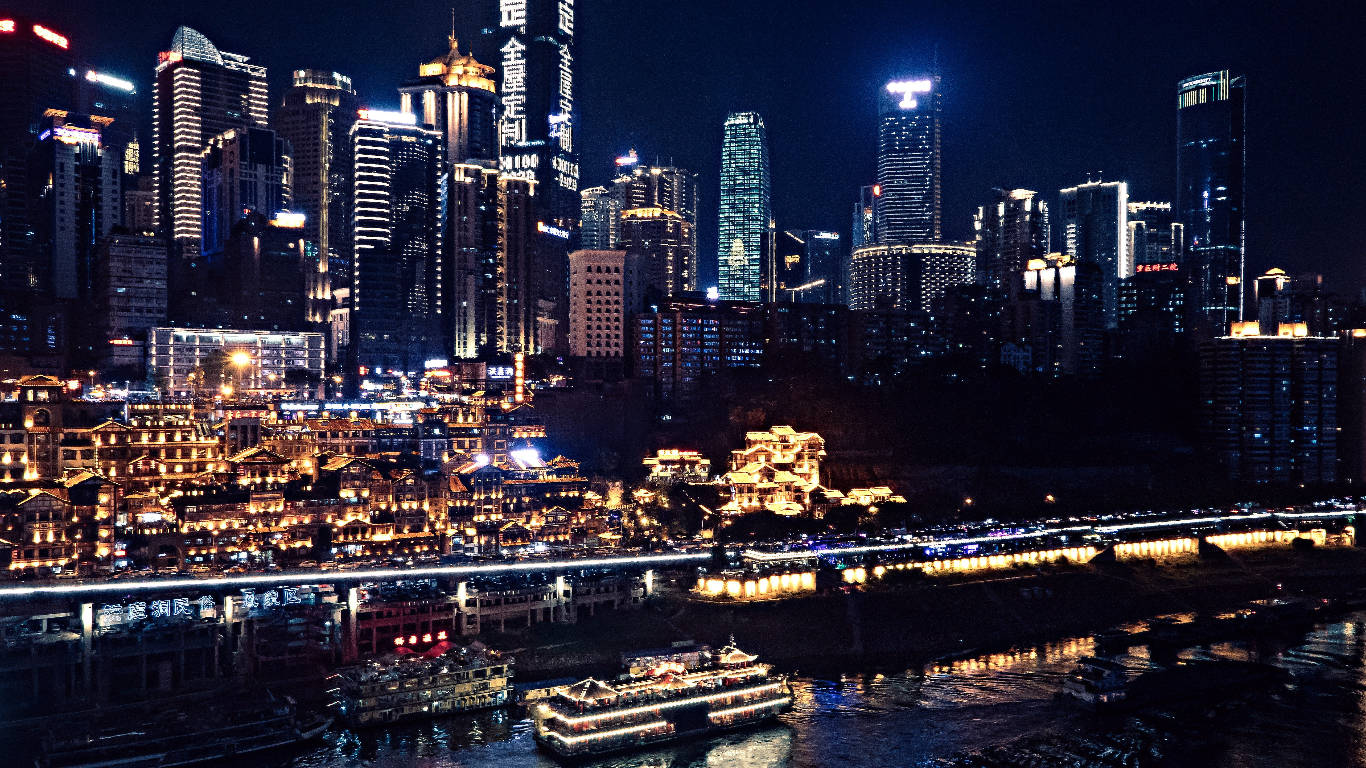 重慶中國霓虹城市景觀 壁紙 — 璀璨的夜景，摩天大樓和傳統建築沿河而立，河上還有燈火通明的船隻。