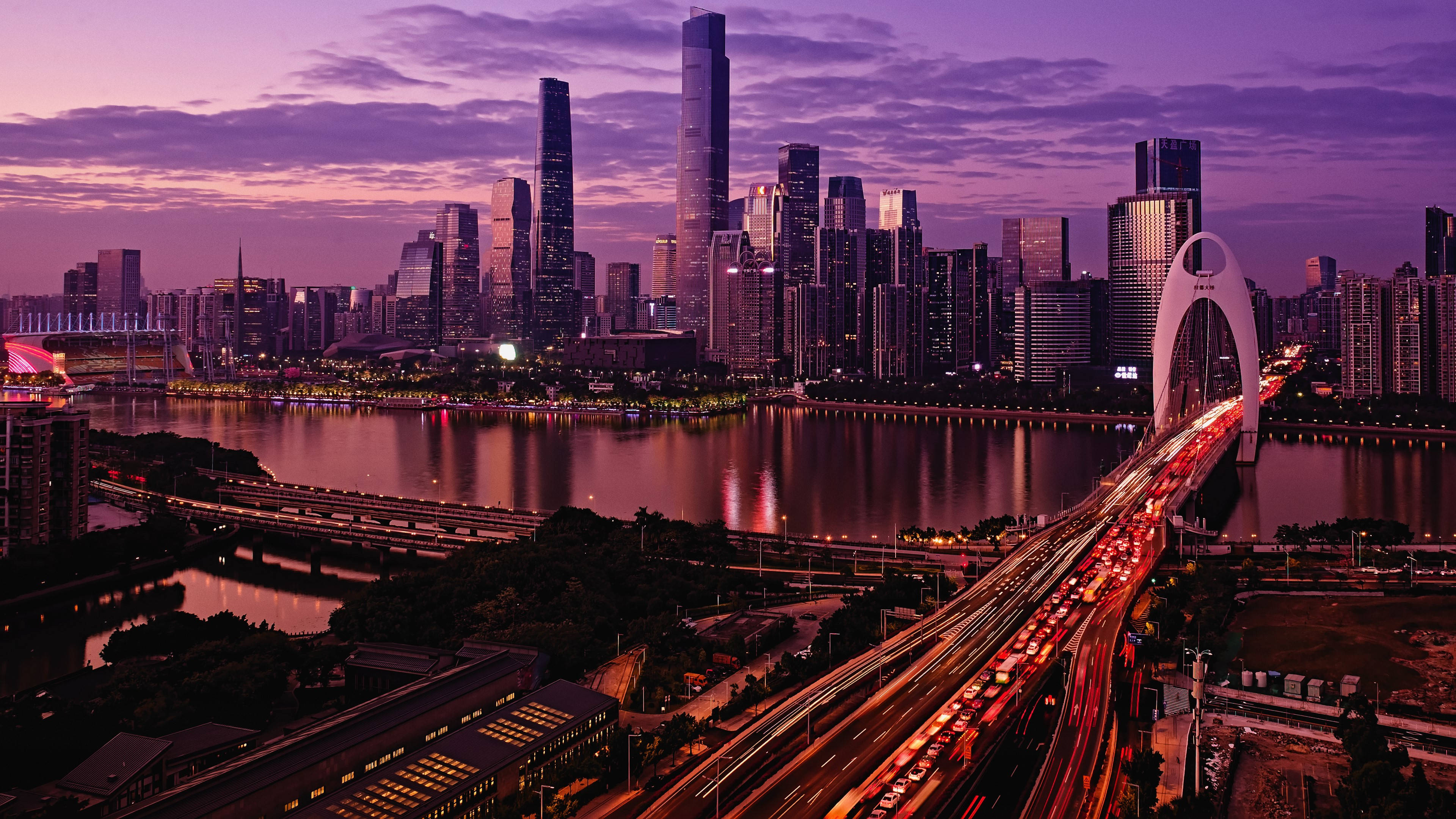 重慶空中交通夜景 壁紙 — 黃昏時分充滿活力的城市天際線，閃爍的摩天大樓和河流反射出紫色和橙色的色調，車流沿著燈火通明的橋樑流動。