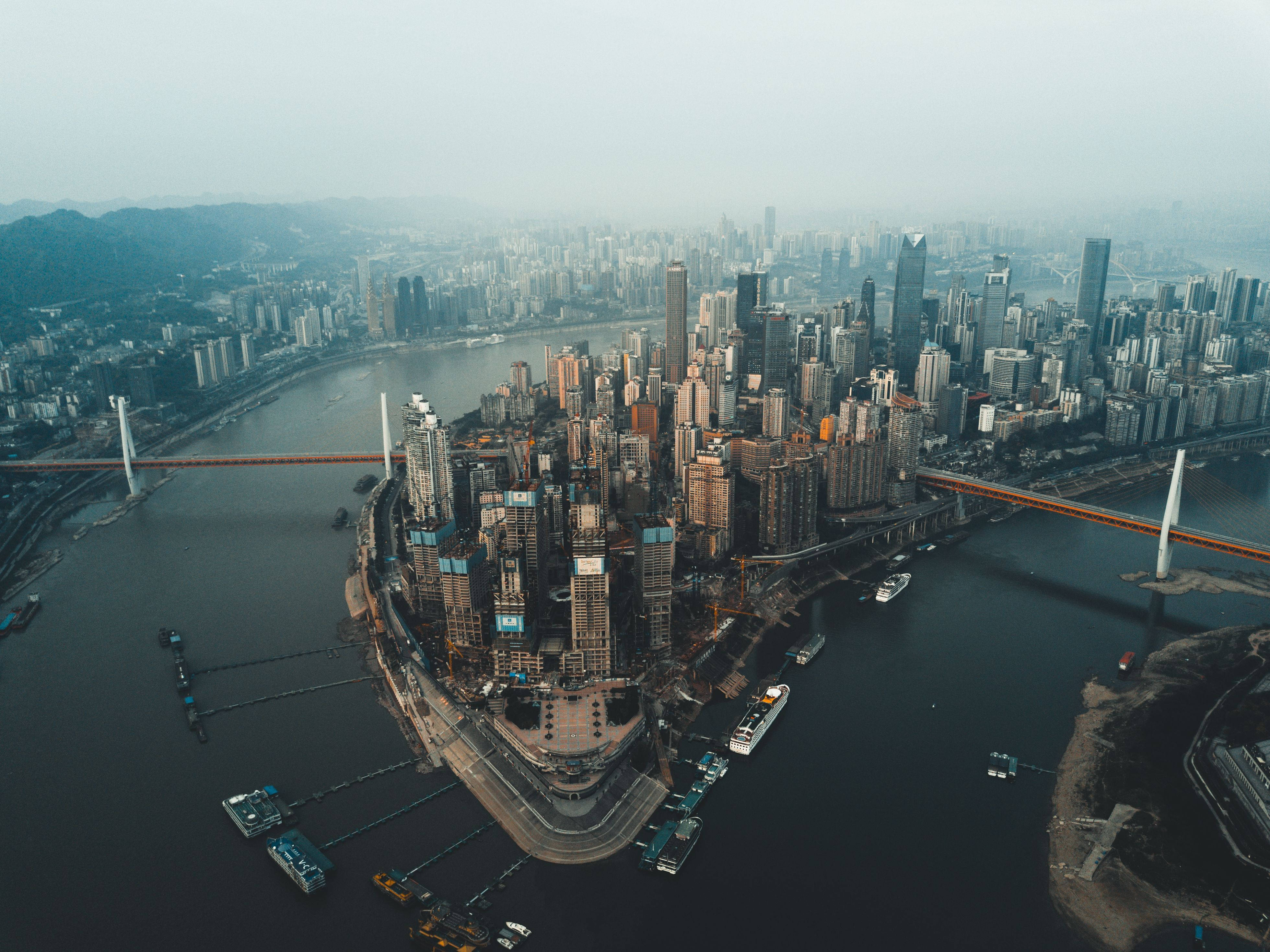 重慶空中鳥瞰都市 壁紙 — 從高空俯瞰，密集的現代城市景觀沿著蜿蜒的河流分佈，橋樑和船隻在朦朧的天空下。