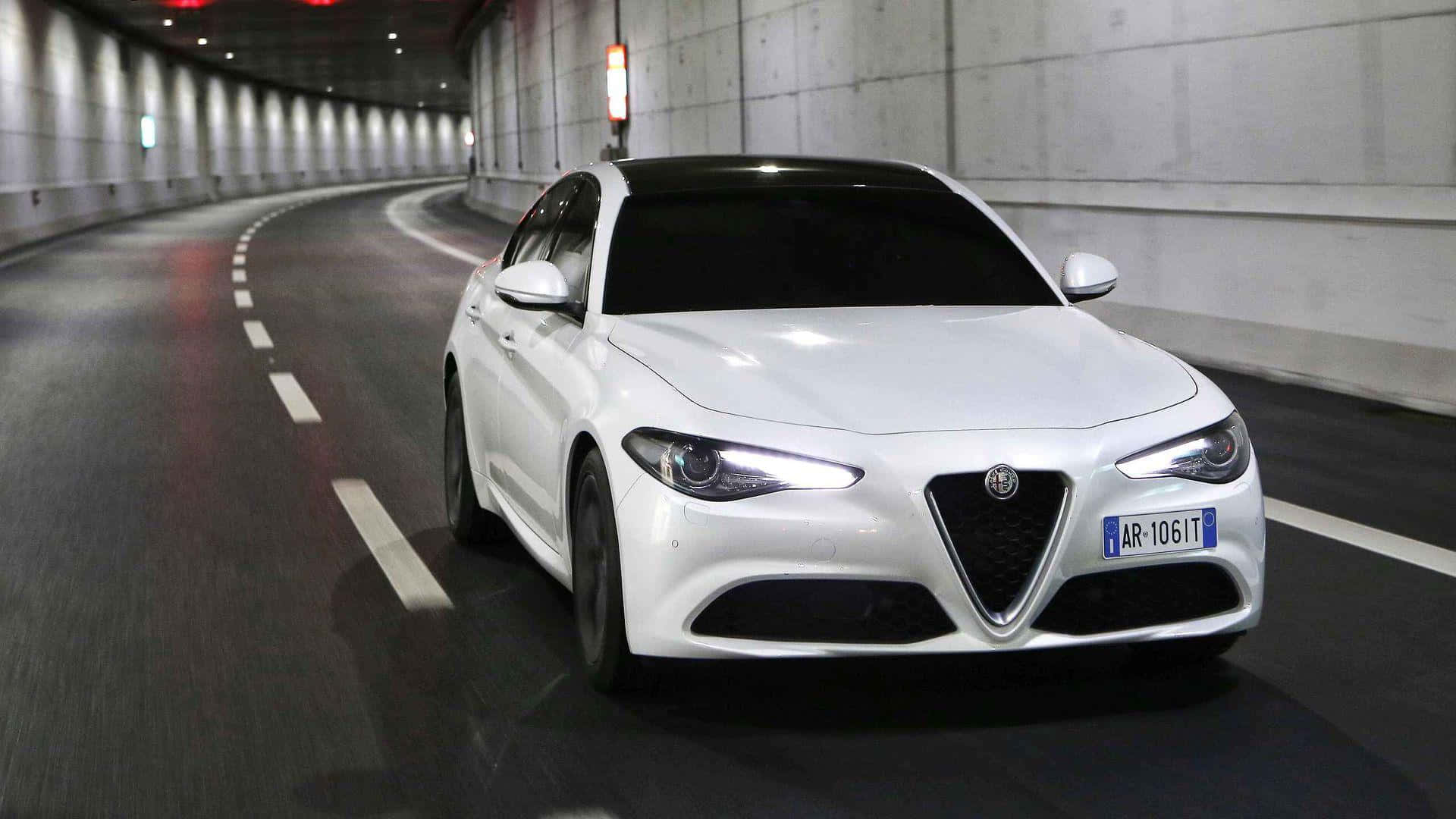 重拾Alfa Romeo的靈魂 壁紙 — 一輛時尚的白色Alfa Romeo房車在燈光昏暗的混凝土隧道中疾馳，車頭燈閃爍。