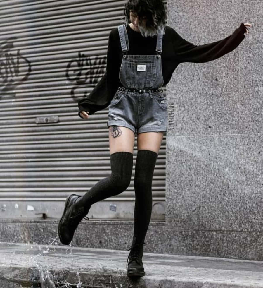 穿著牛仔工人褲和靴子的人，在塗鴉牆附近跳過濕漉漉的人行道。