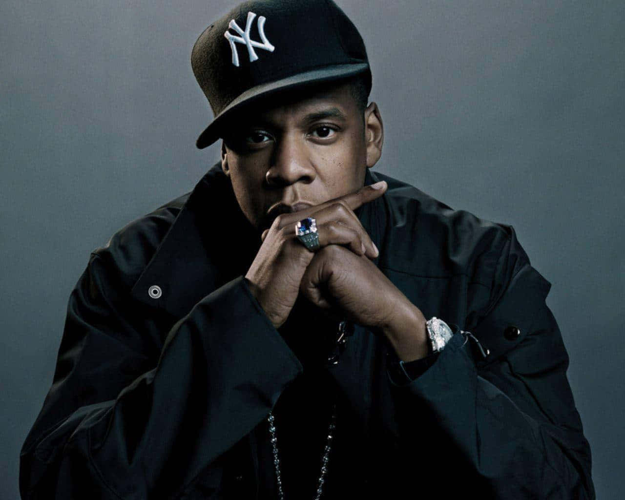 重返90年代：黑人時尚、音樂與文化 壁紙 — Beyoncé 雙手交疊在下巴下方，戴著黑色NY帽和外套，在灰色背景前凝視。
