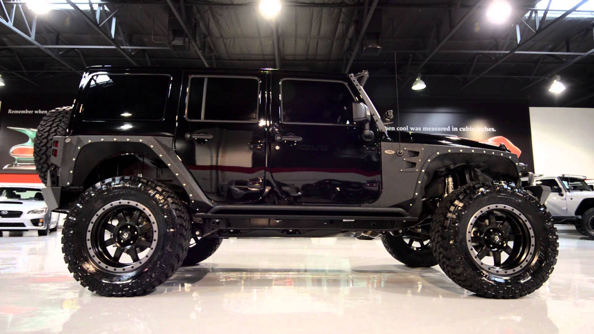 展廳地板上的黑色升高底盤Jeep Wrangler，配備大輪胎和鍍鉻裝飾。