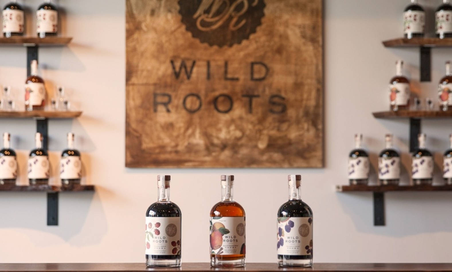 三瓶 Wild Roots 烈酒陳列在吧檯上，後面有架子和木牌。