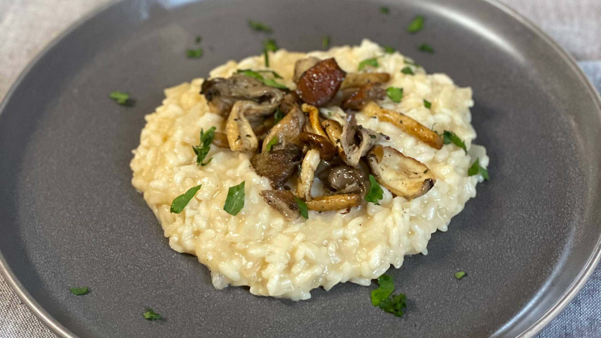 野生蘑菇燉飯 壁紙 — 一道奶油蘑菇燴飯，飾以新鮮歐芹，優雅地擺放在磨砂灰色盤子上。
