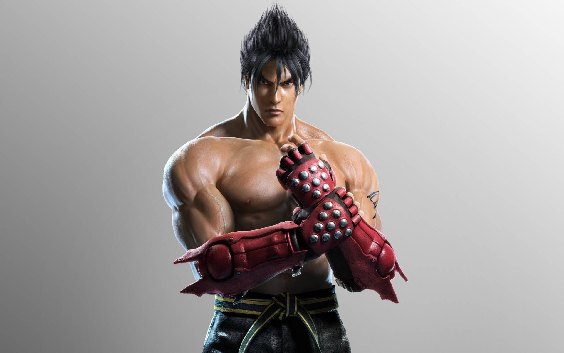 金· Kazama 灰色背景 壁紙 — 一個肌肉發達的動漫戰士，擁有尖刺黑髮和紅色尖刺護手，在純灰色背景前擺出戰鬥姿勢。