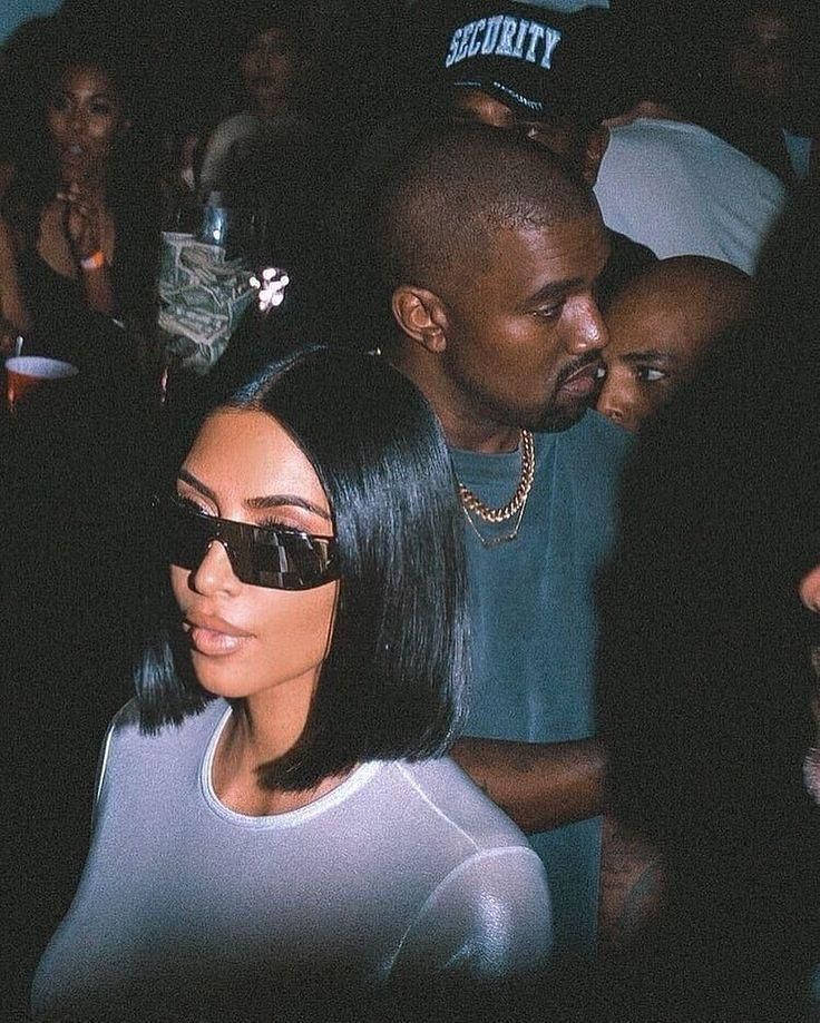 Kim Kardashian 在夜間派對上戴著太陽眼鏡，Kanye West 在附近。