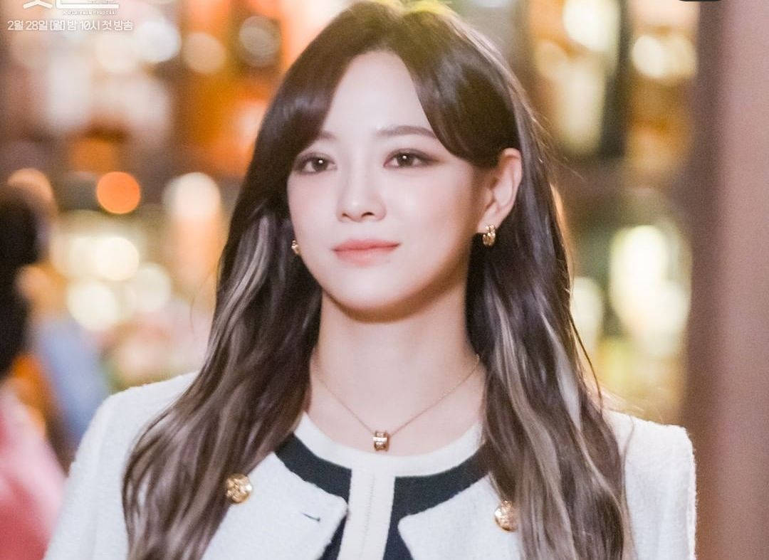 金世正飾演《業務提案》Ha-ri 壁紙 — 一位長黑髮、戴金耳環的年輕女性在溫暖燈光的城市夜景中，身後有模糊的散景燈光，溫柔地微笑。
