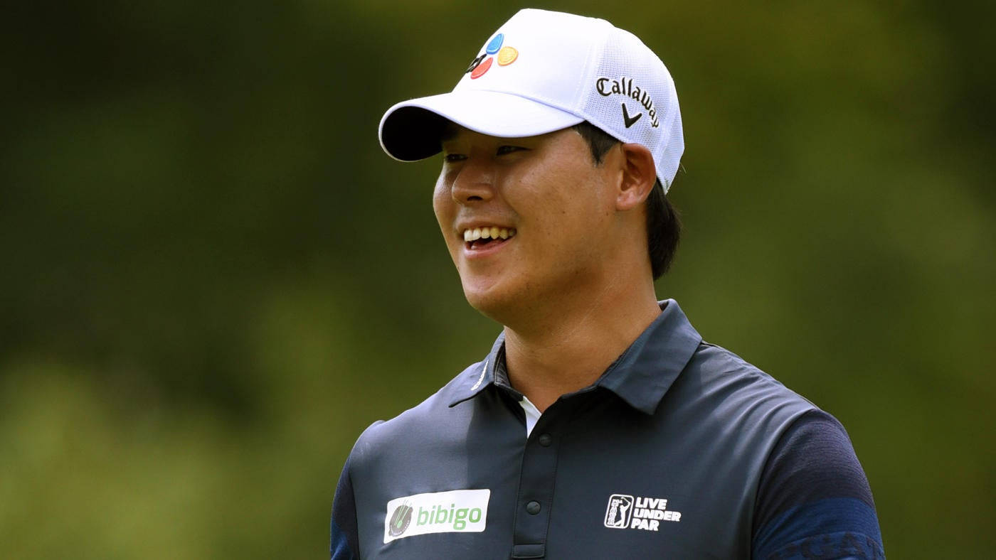 金世煐溫柔微笑 壁紙 — 一位戴著白色 Callaway 帽子和深色 Polo 衫的高爾夫球手微笑著站在模糊的綠色背景前。